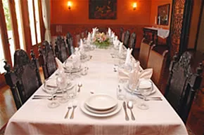 Un comedor formal presenta una mesa larga con mantelería blanca y vajilla.
