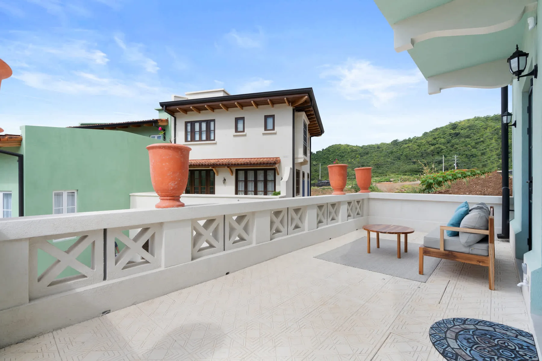 Una terraza exterior embaldosada ofrece vistas a casas cercanas y colinas verdes.