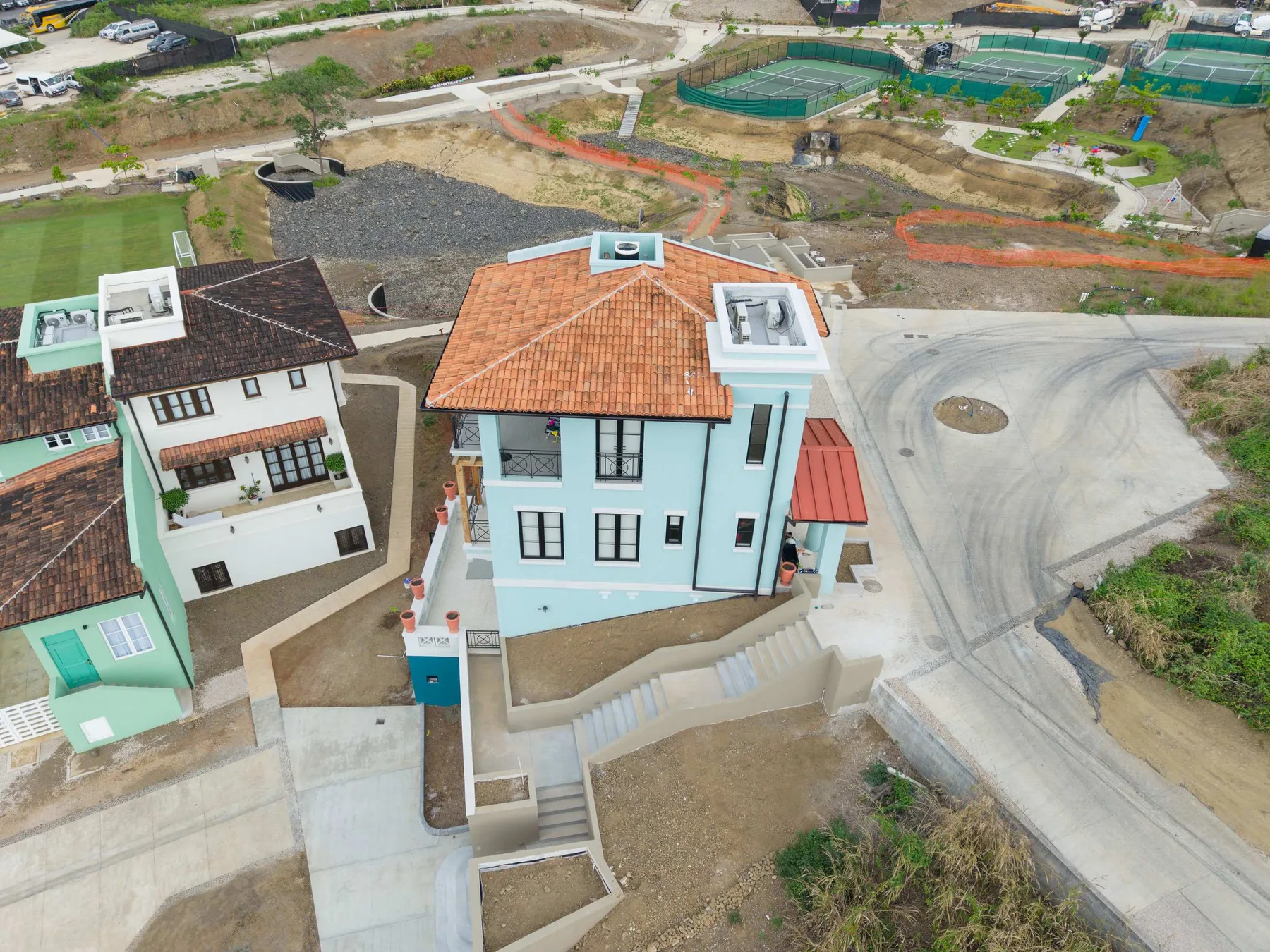 Una vista aérea muestra dos casas vecinas junto a una carretera curva y un terreno en construcción.