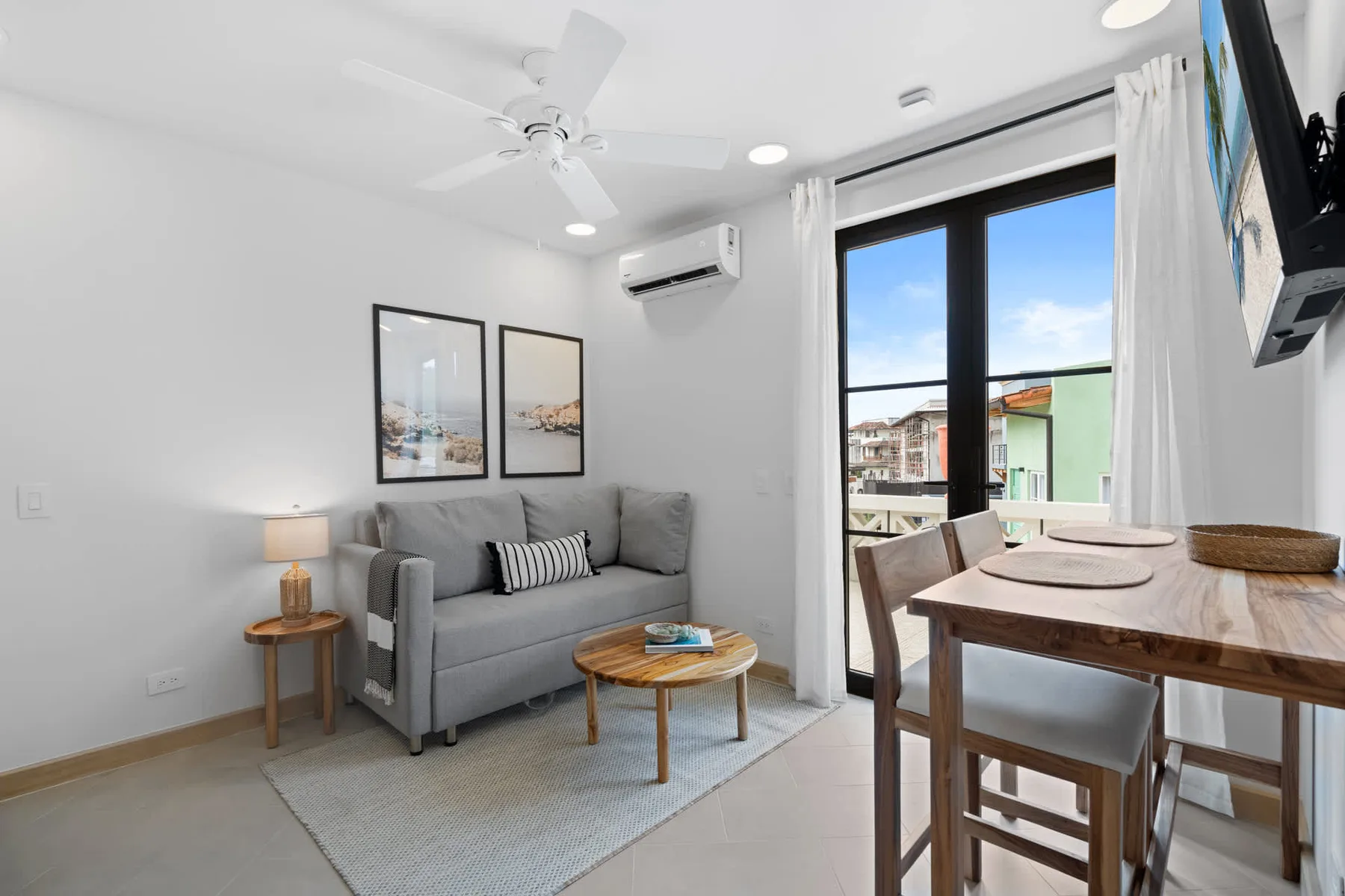 Una sala de estar y comedor con asientos grises y una mesa de madera junto a una ventana grande.