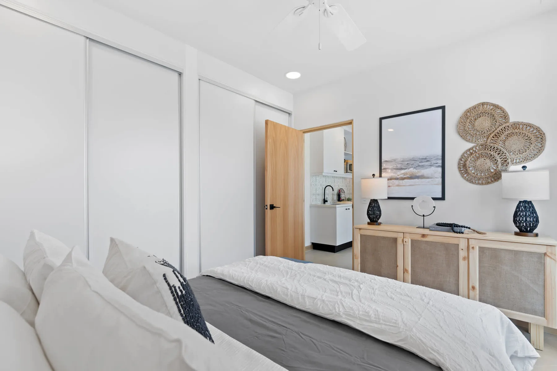Un dormitorio luminoso con una cama, una cómoda de madera y una imagen costera enmarcada.