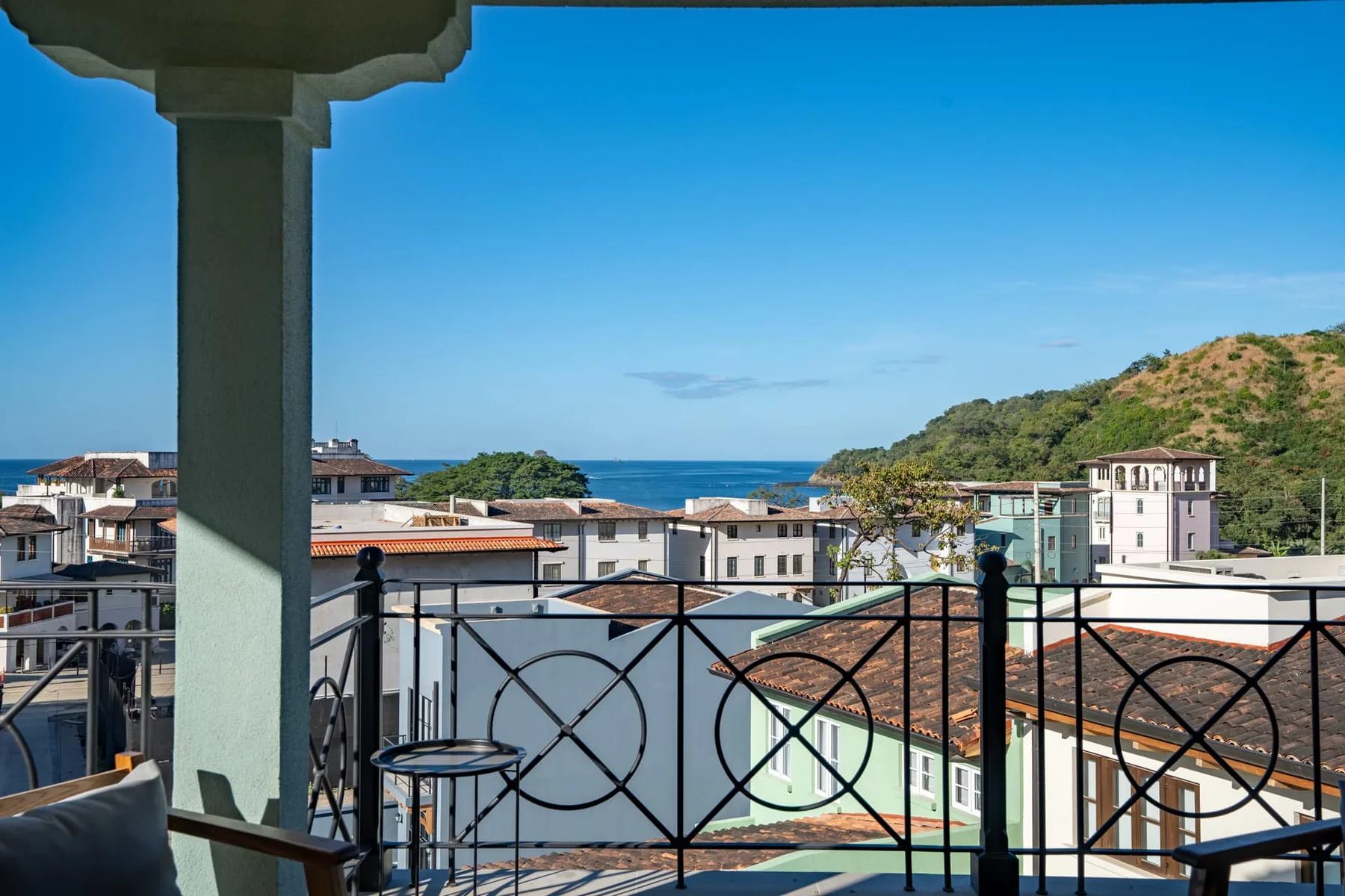 Un balcón tiene vistas a edificios cercanos, el mar y una colina verde.
