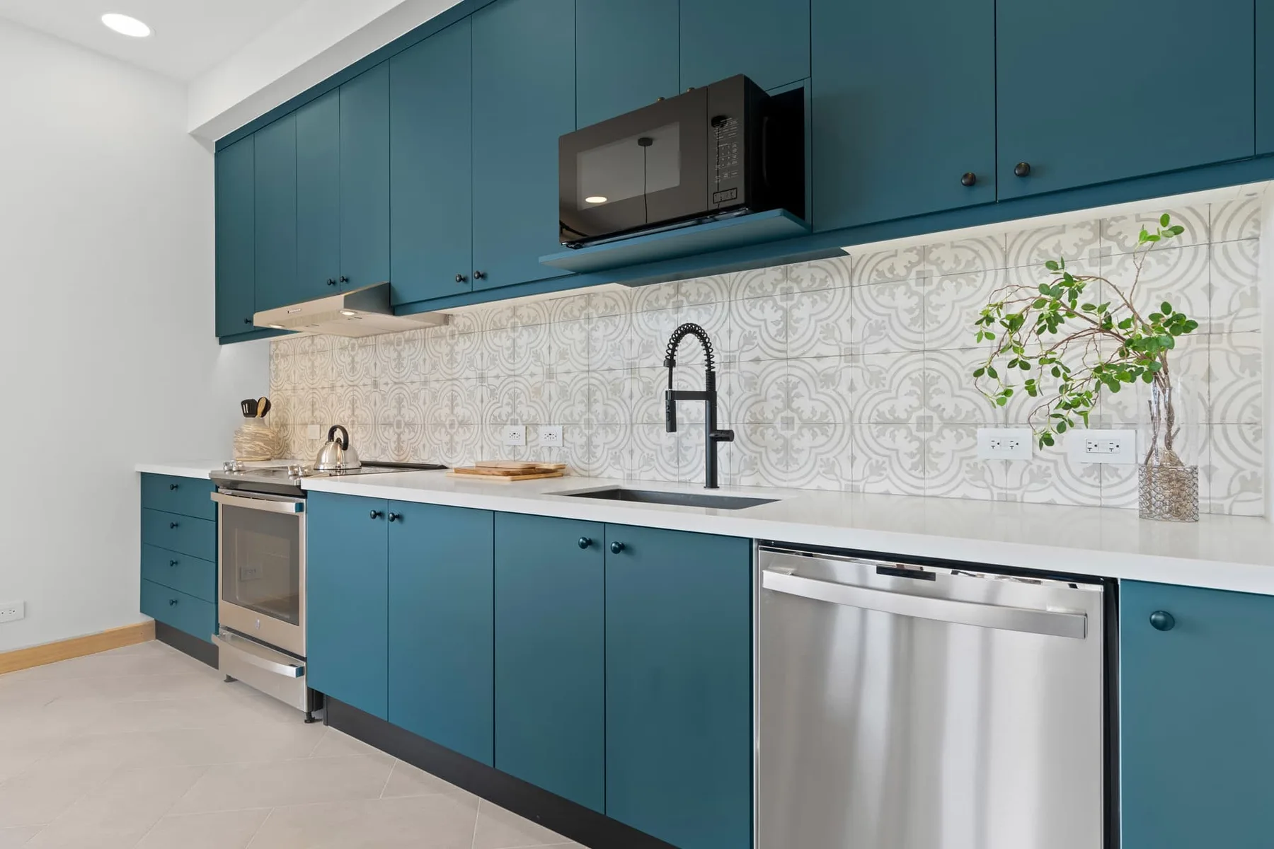 Una cocina moderna con gabinetes verde azulado, un salpicadero estampado y electrodomésticos de acero inoxidable.