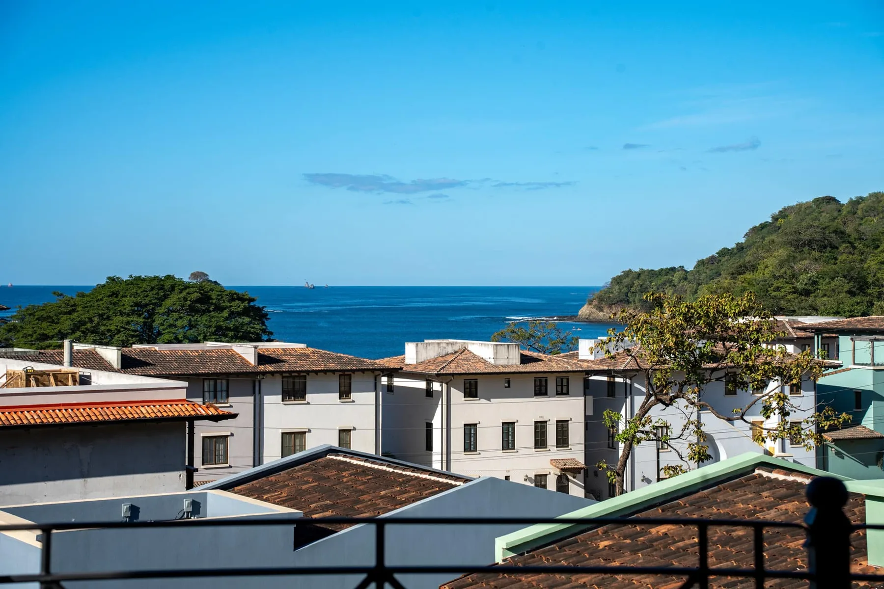 Vista costera sobre edificios cercanos hacia el mar azul y una colina verde.