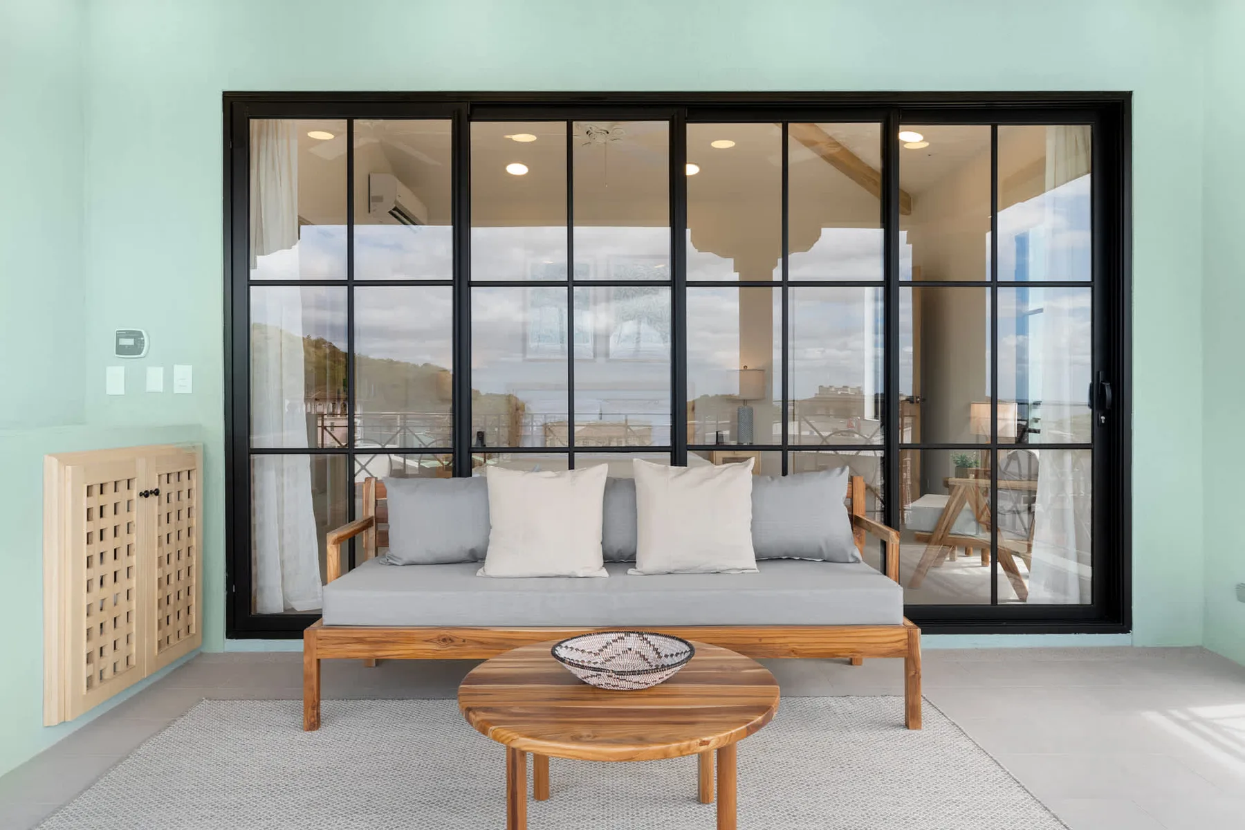 Una zona de estar da a grandes ventanas con marcos negros, con una mesa baja de madera delante.