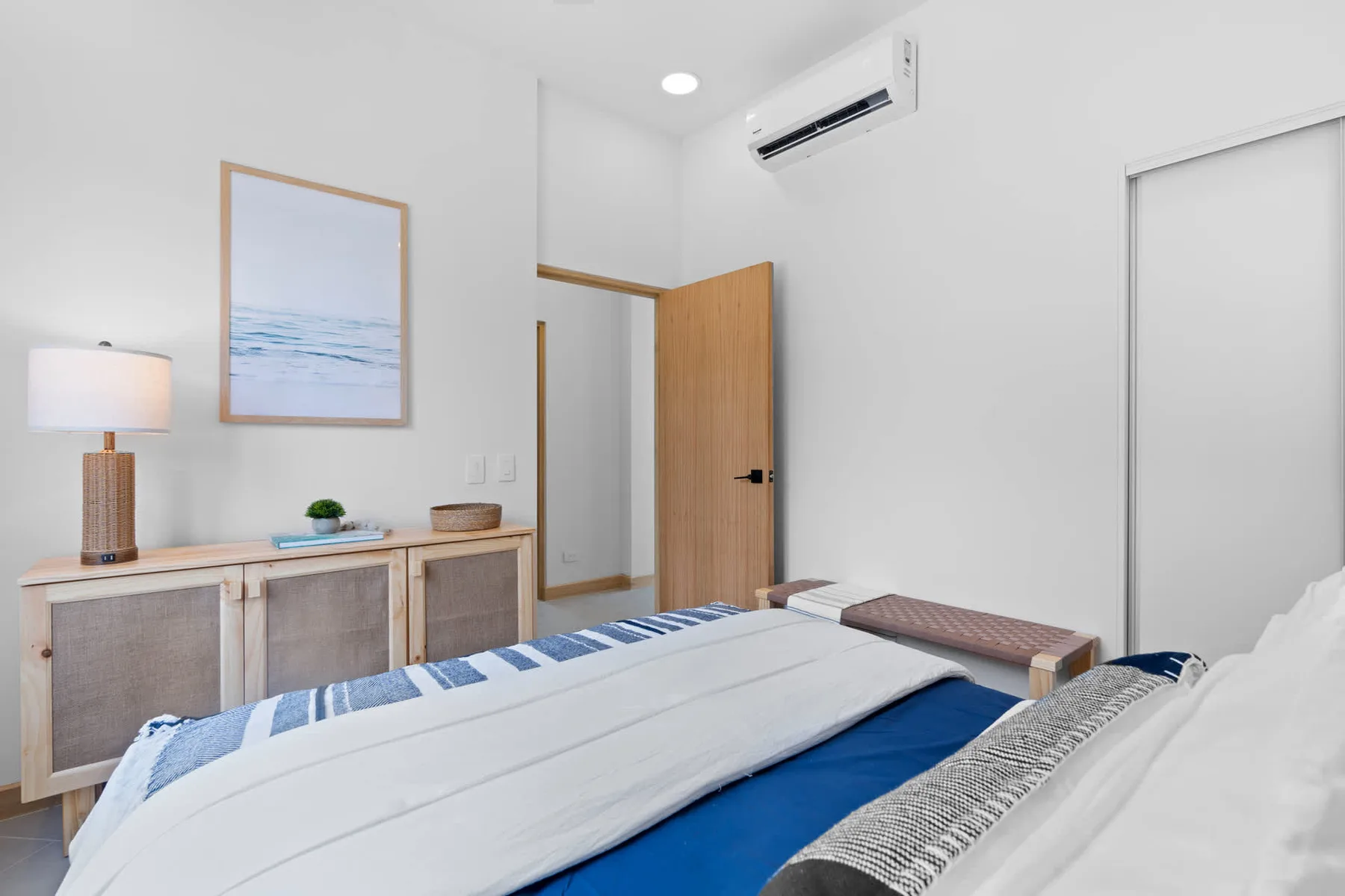 Un dormitorio luminoso con una cama bien tendida y un cuadro del océano.