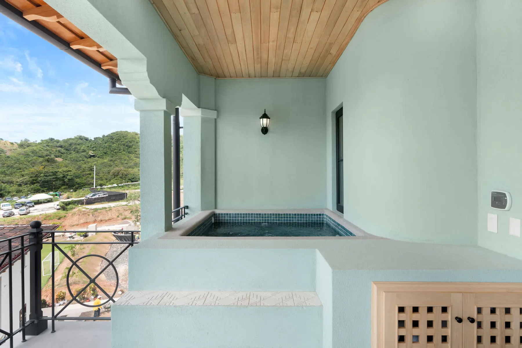 Un balcón cubierto con una pequeña piscina y vistas a colinas verdes.
