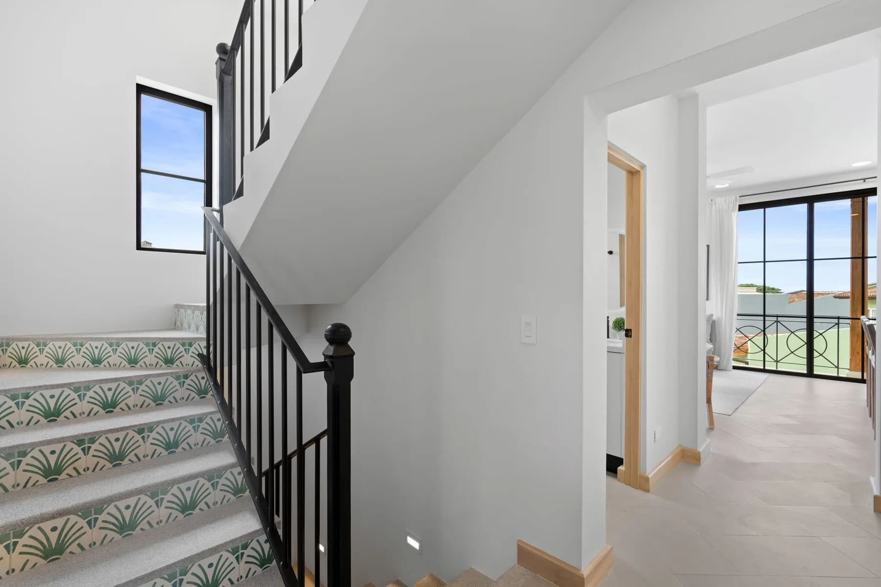 Una escalera con peldaños de azulejos estampados y barandilla negra conduce a un pasillo luminoso.