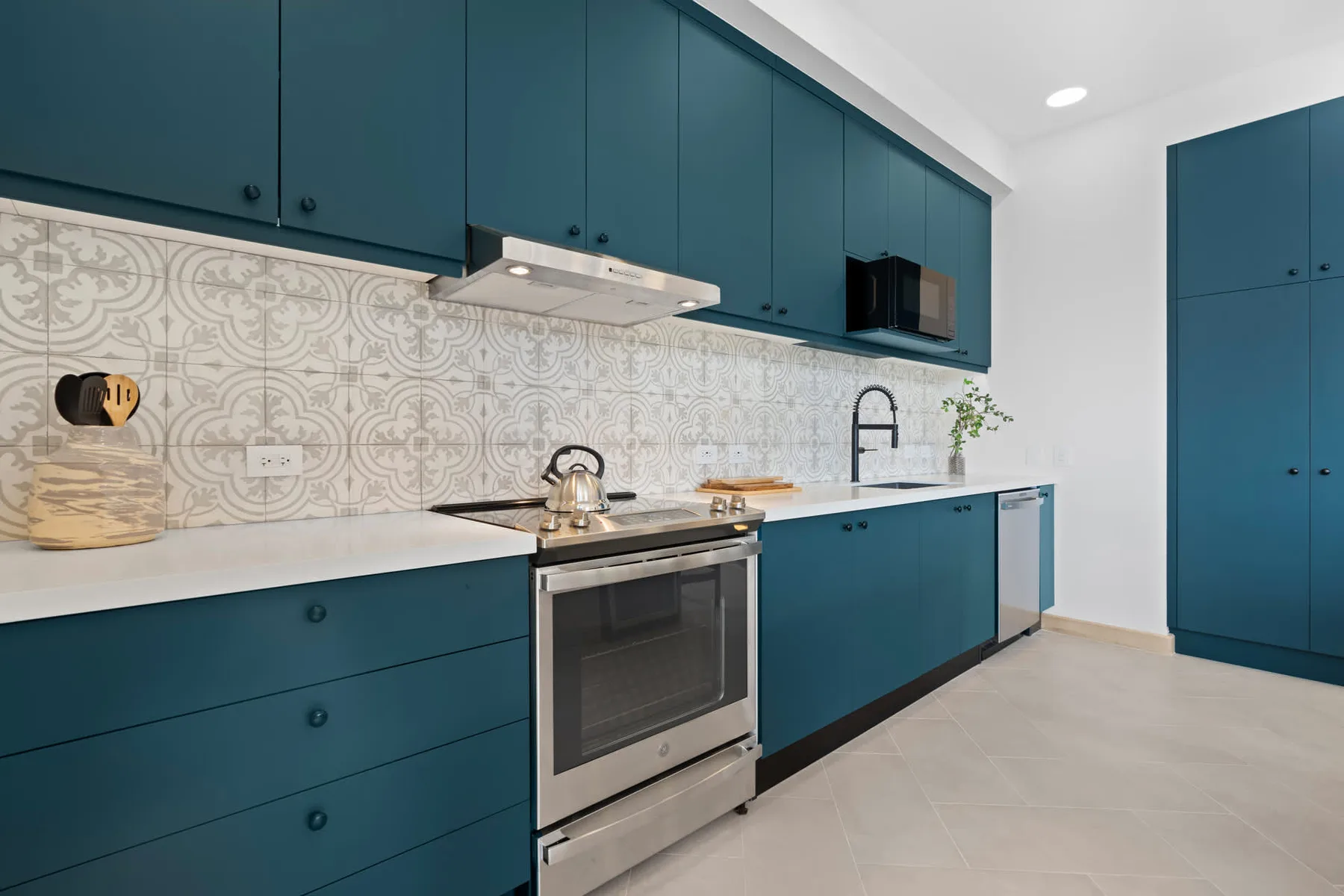Una cocina moderna con gabinetes verde azulado, estufa y salpicadero estampado.