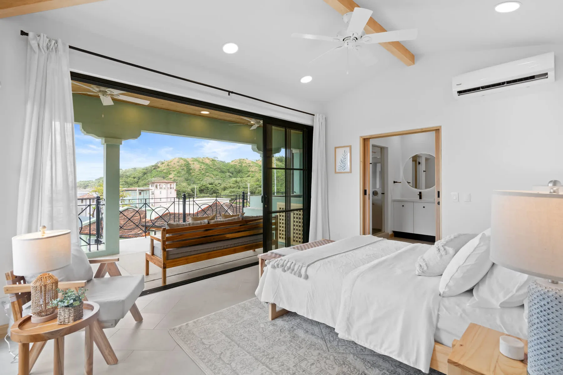 Un dormitorio luminoso con ropa de cama blanca y una gran ventana que da a un balcón.