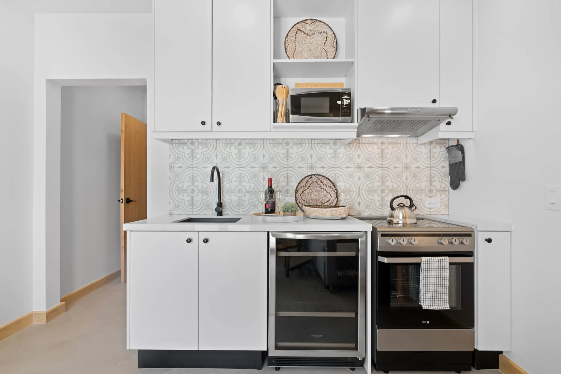 Una cocina blanca luminosa con salpicadero estampado y electrodomésticos integrados.