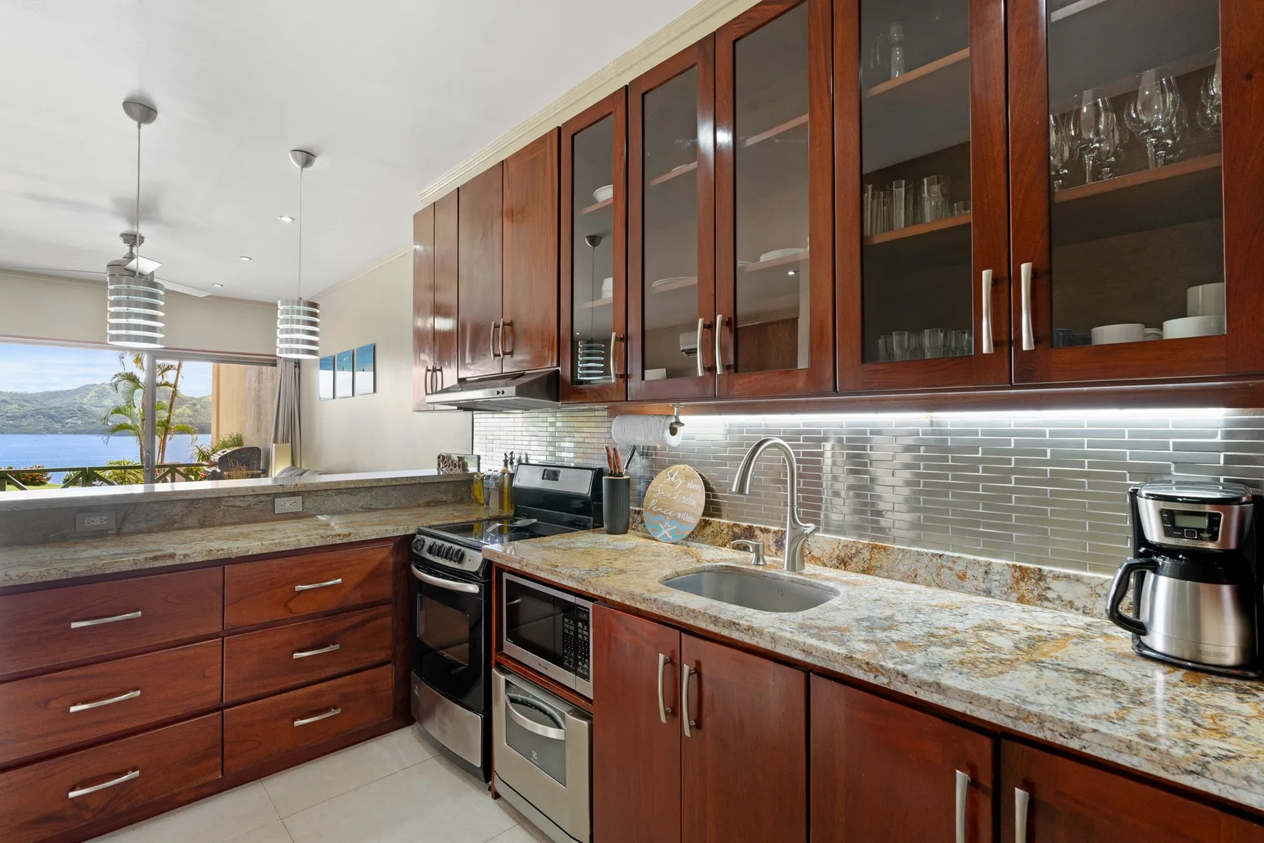 A modern kitchen with wood cabinets, stone countertops, and a window overlooking the water.