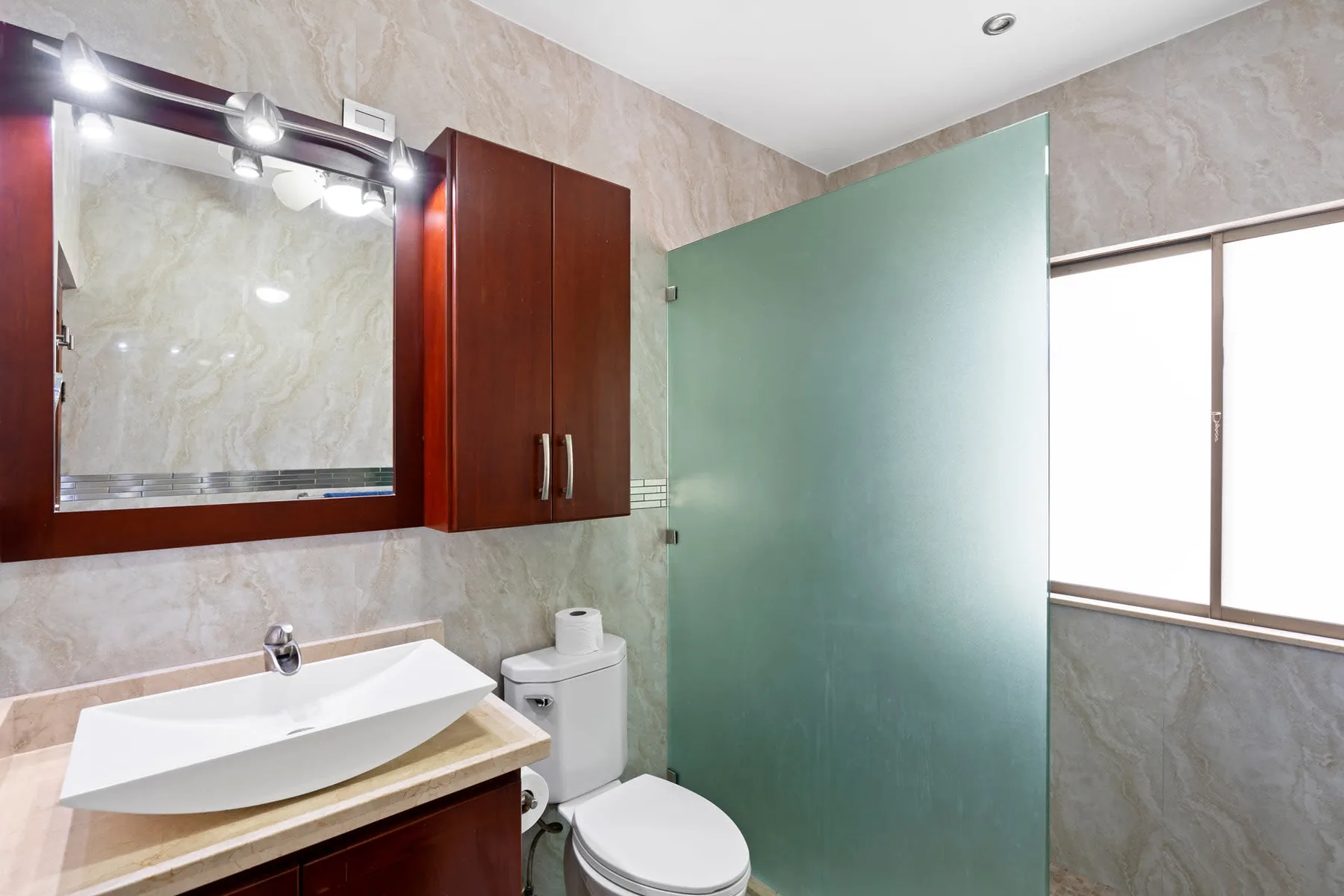 A bathroom with a sink, toilet, and frosted glass shower panel.