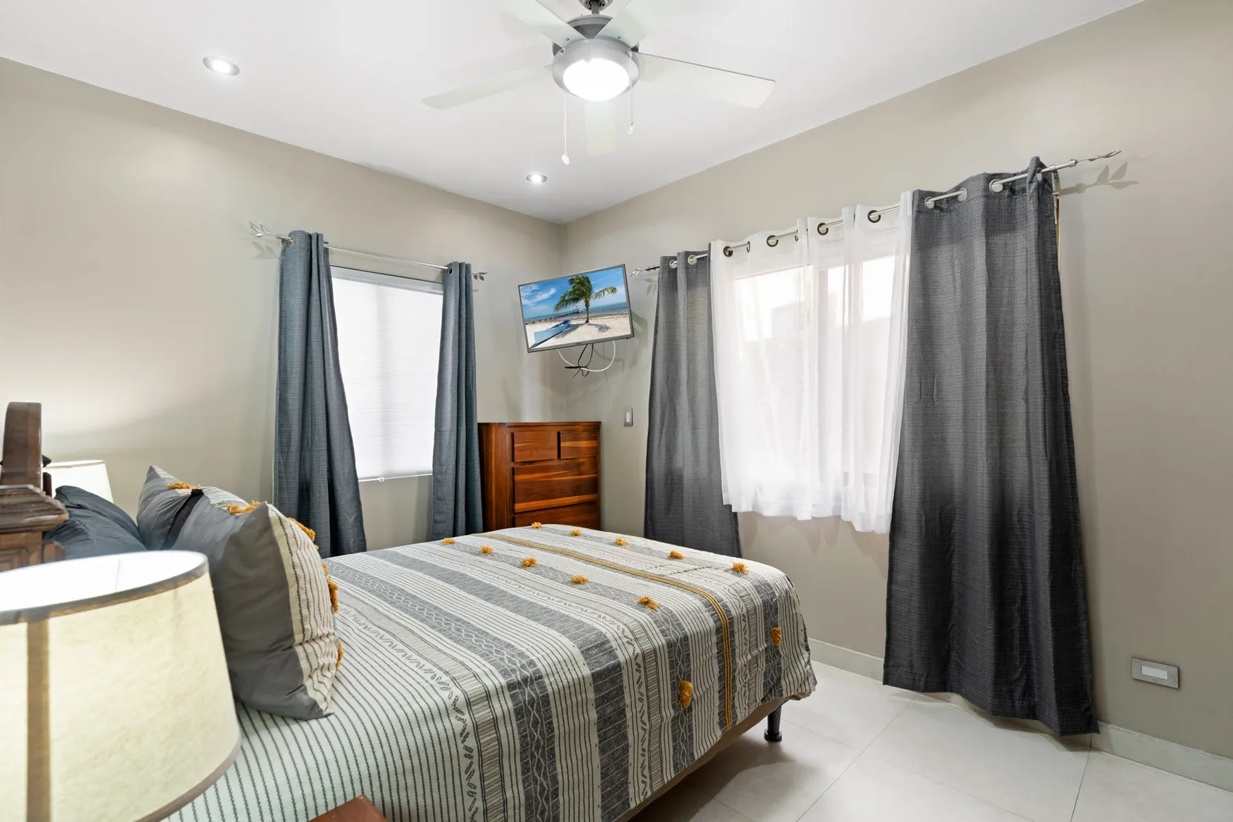 A bedroom with a bed, curtained windows, and a small television.