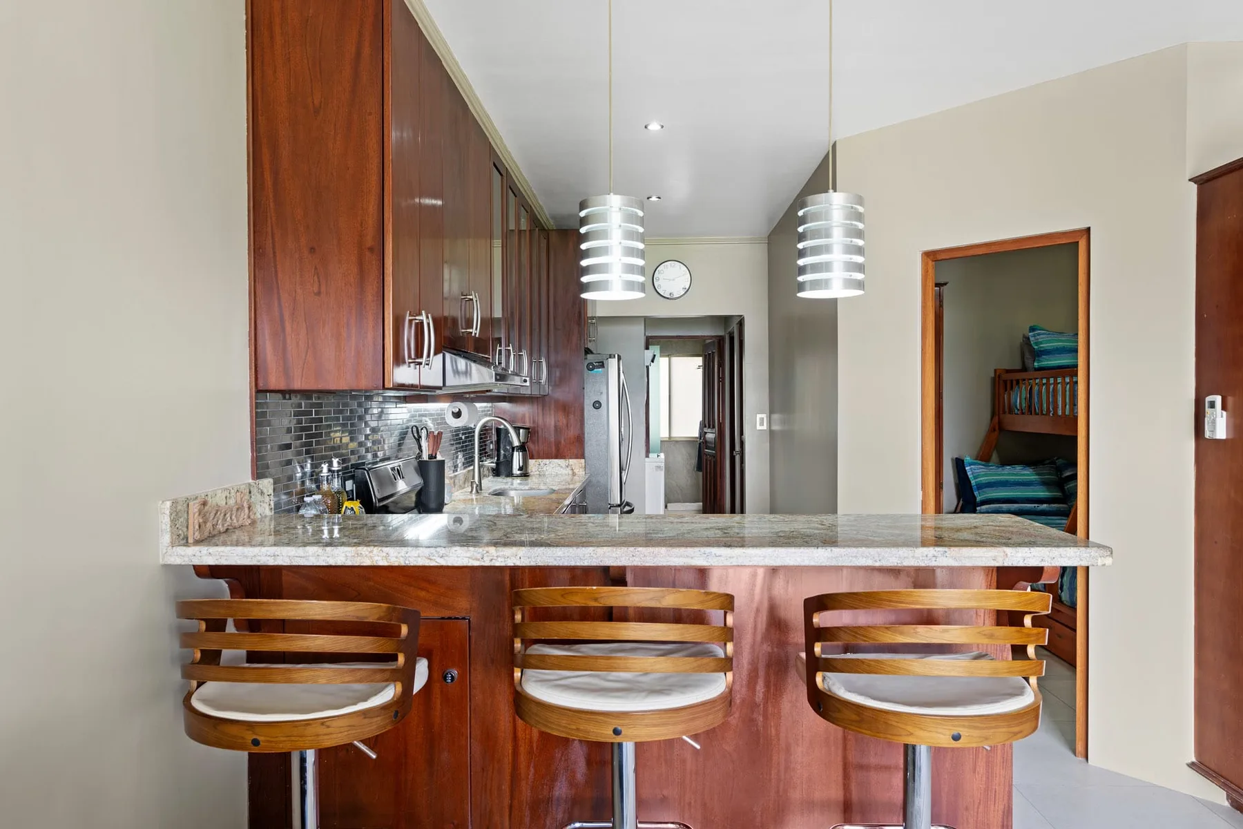 A kitchen counter with wooden bar seating and overhead pendant lights.