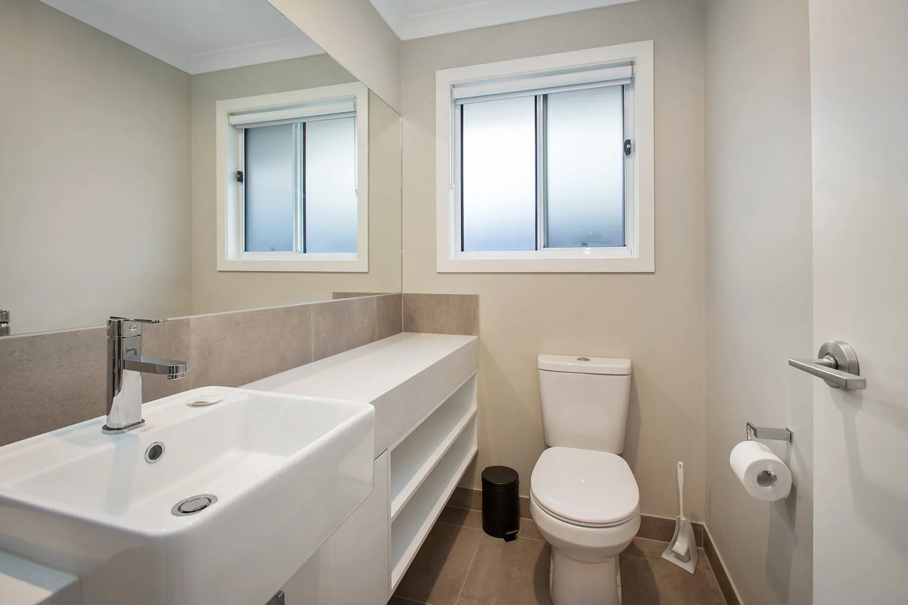 A bathroom with a sink, toilet, and two windows.