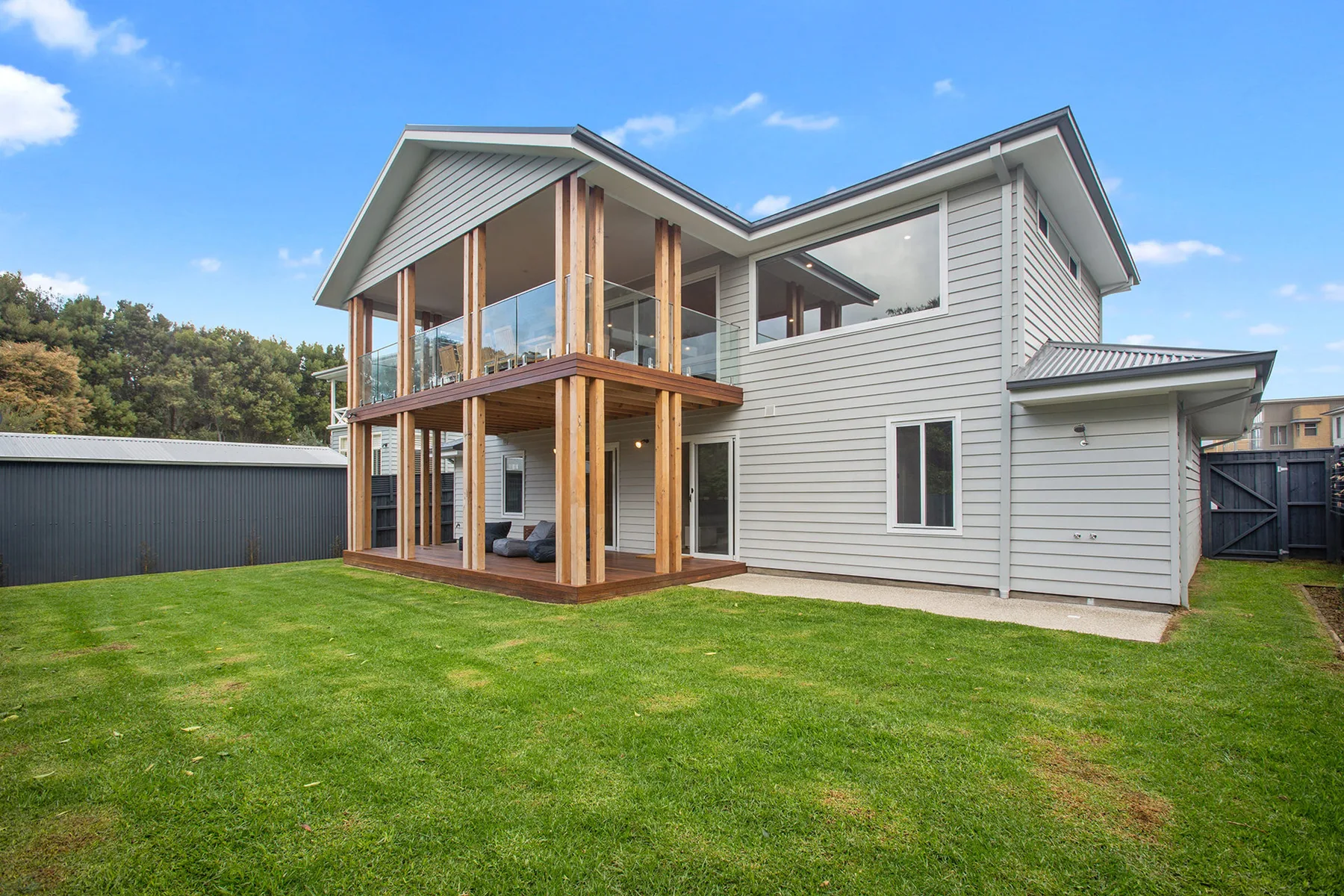 Modern two-story house with a covered balcony overlooking a green lawn.