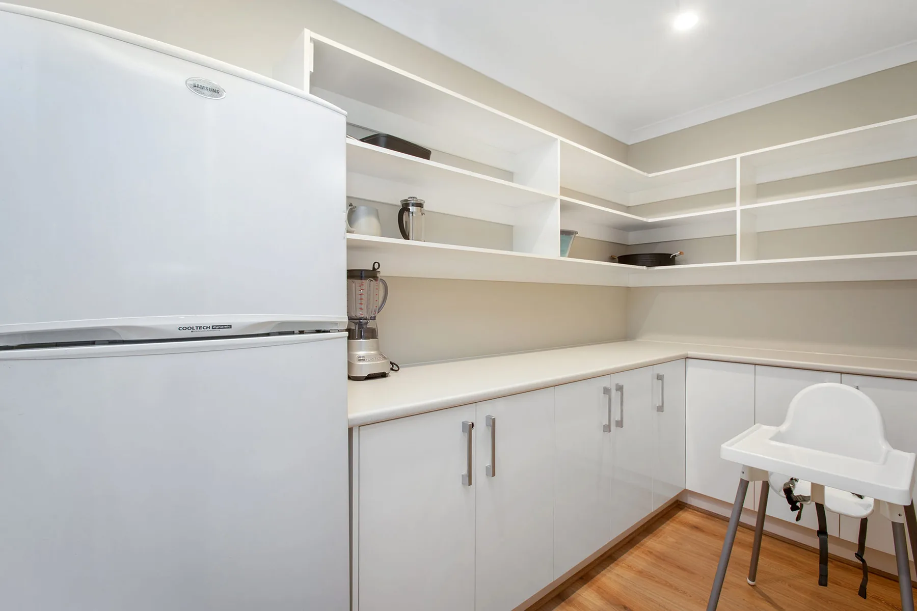 A bright kitchen with white cabinetry, open shelves, and a refrigerator.