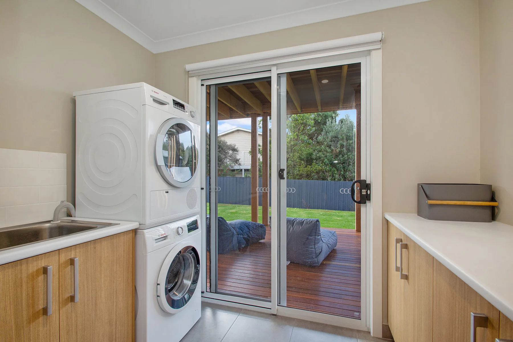 A laundry room with stacked washing machines beside sliding glass doors to a deck.
