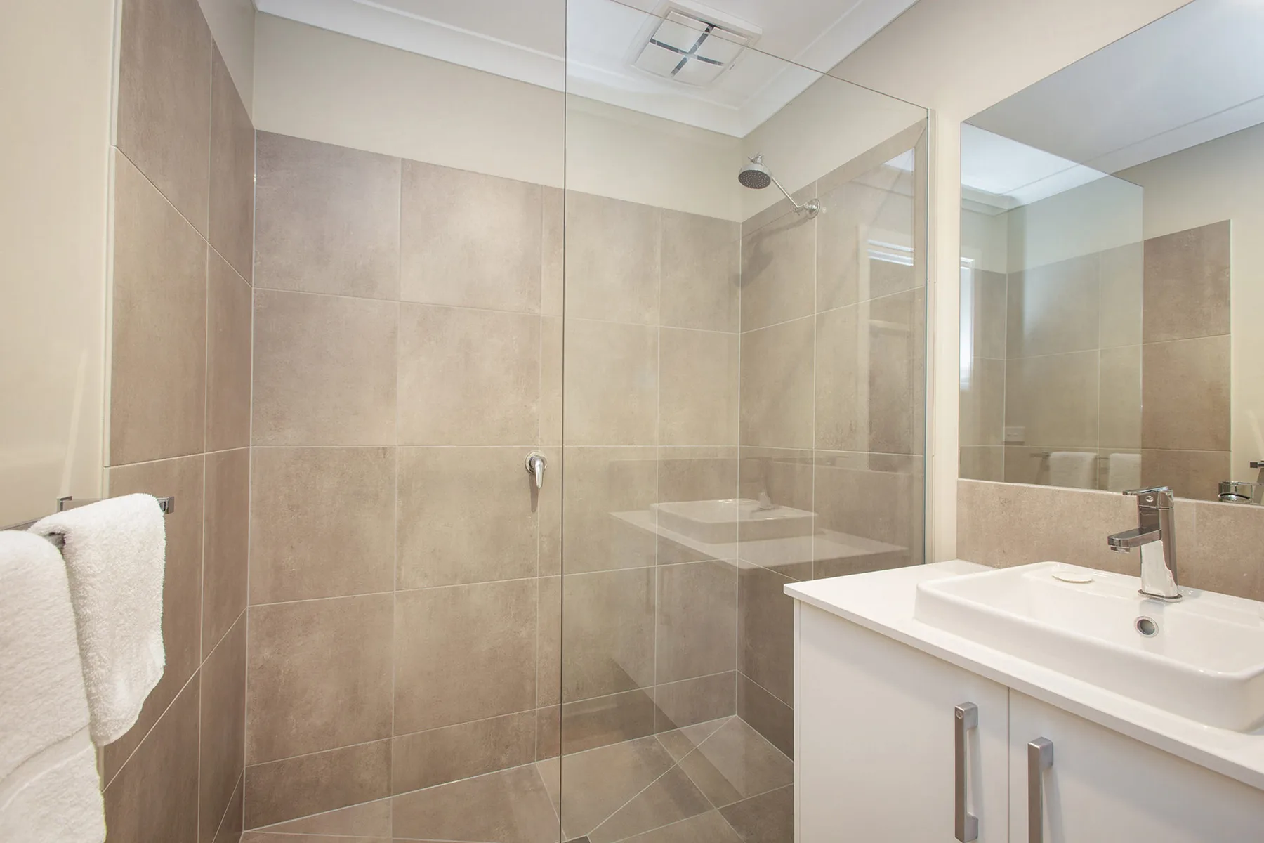 A tiled bathroom with a glass shower and a white vanity.