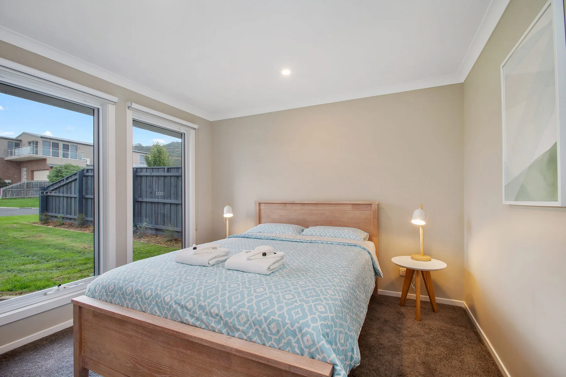 A bedroom with a bed beside tall windows overlooking a fenced yard.
