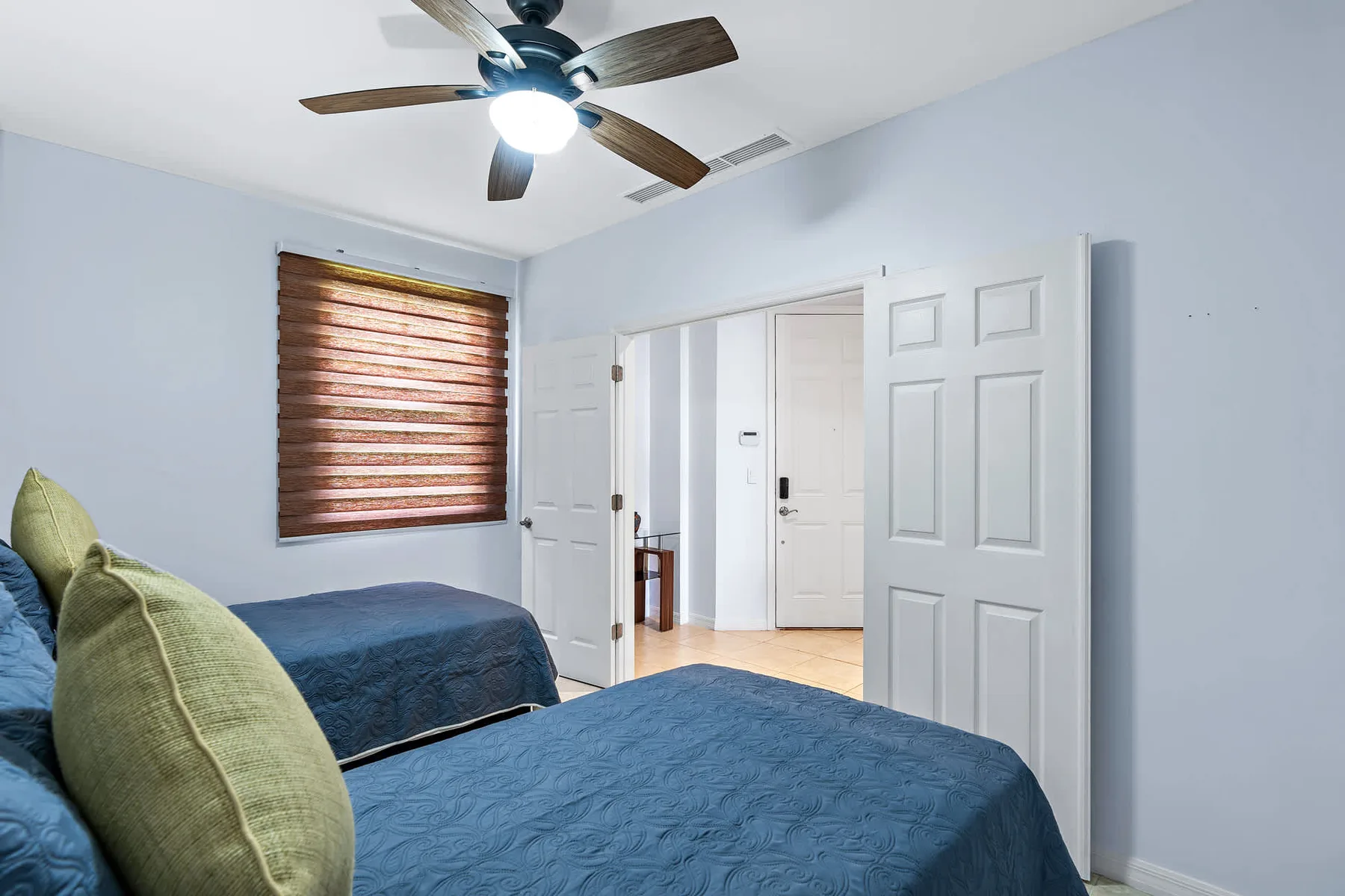 Un dormitorio con ropa de cama azul, almohadas verdes y una ventana con persiana de madera.
