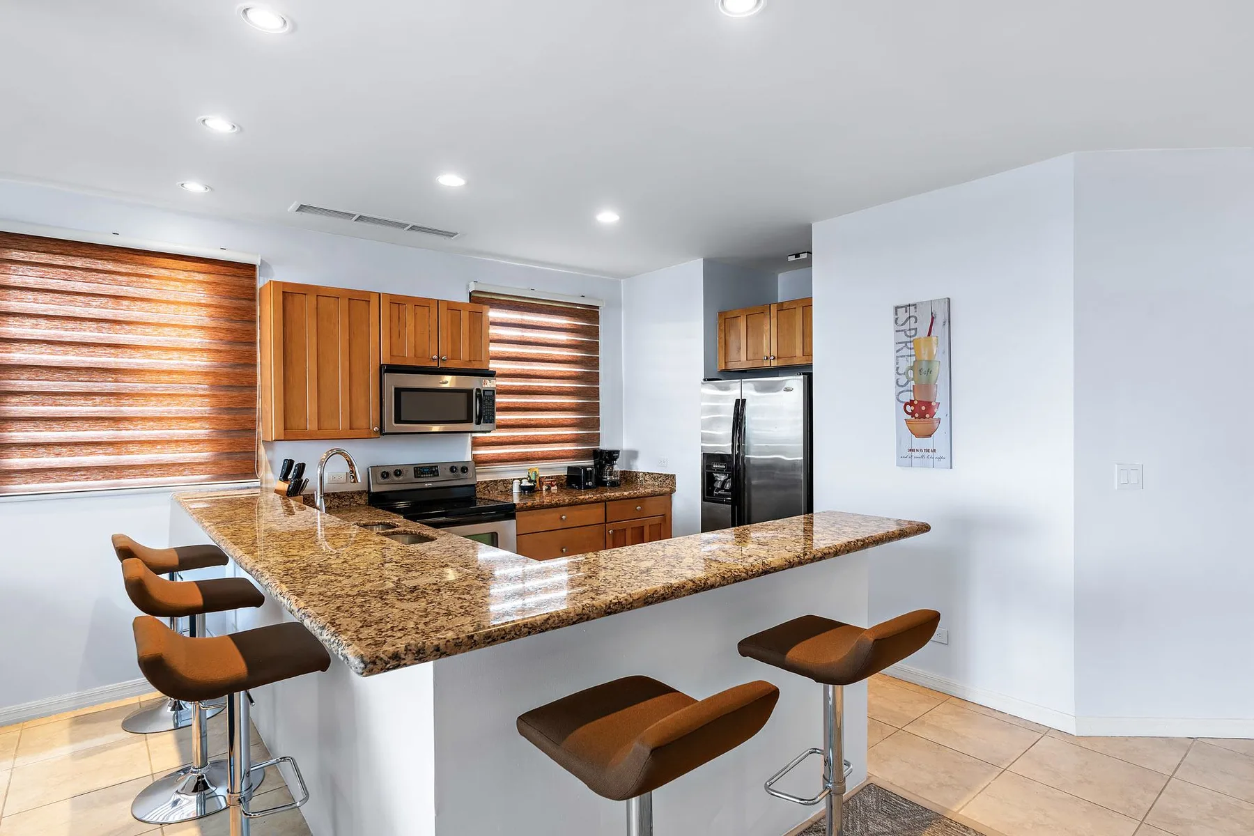 Una cocina luminosa con una isla de granito, gabinetes de madera y asientos de bar.
