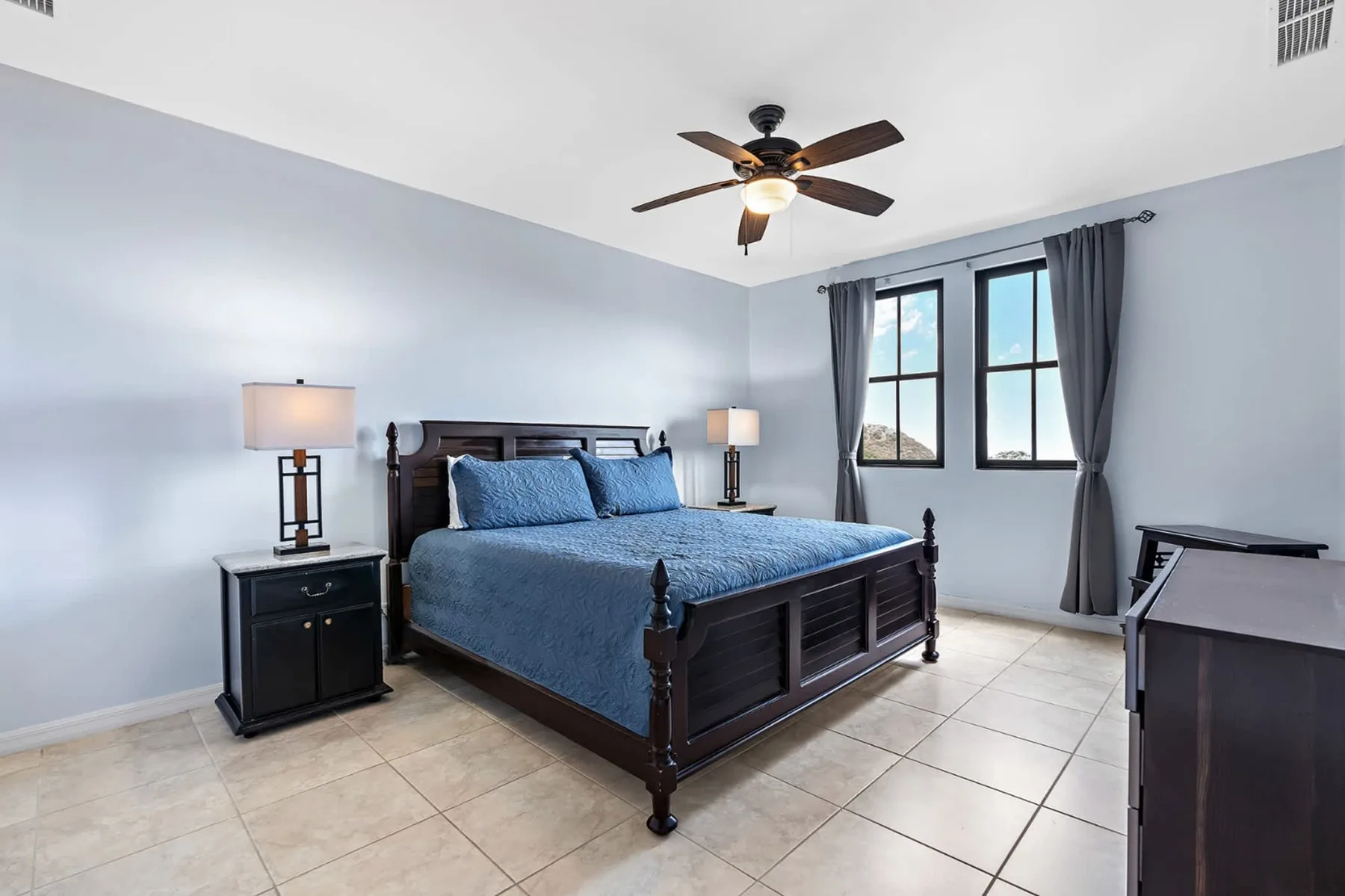 Un dormitorio con una cama de madera oscura vestida con ropa de cama azul y una ventana.