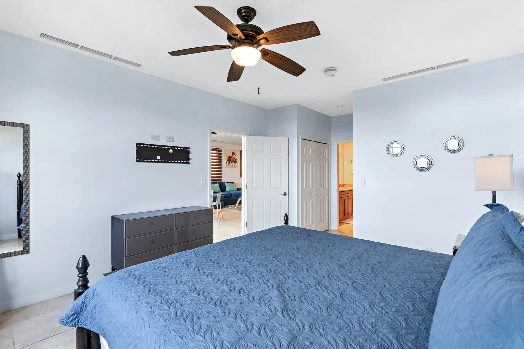 Un dormitorio con una cama cubierta de azul, una cómoda y un ventilador de techo.