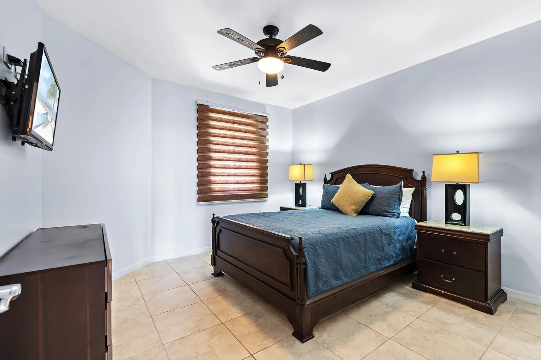 Un dormitorio con una cama de madera oscura, mesitas de noche y un ventilador de techo.