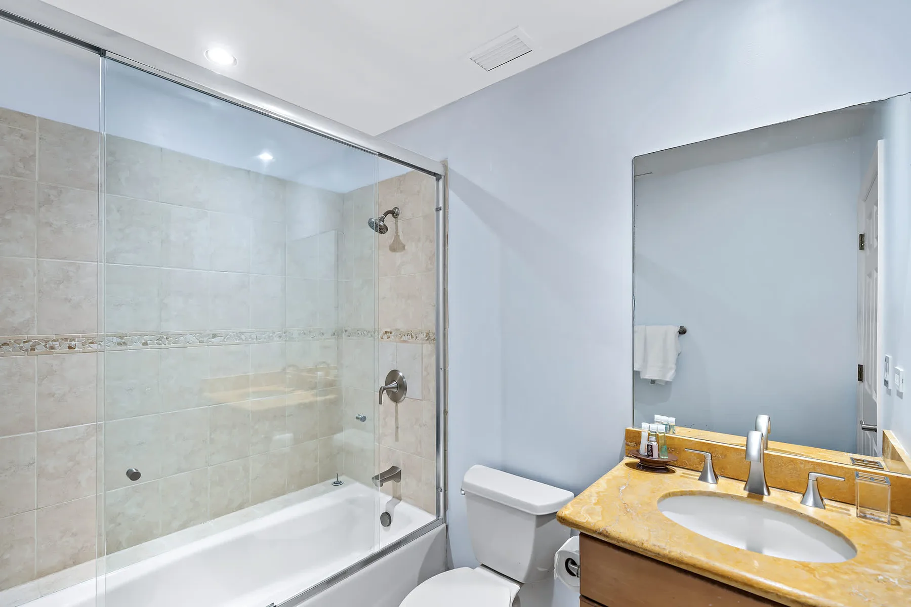 Un baño alicatado con ducha de vidrio, bañera y lavabo.