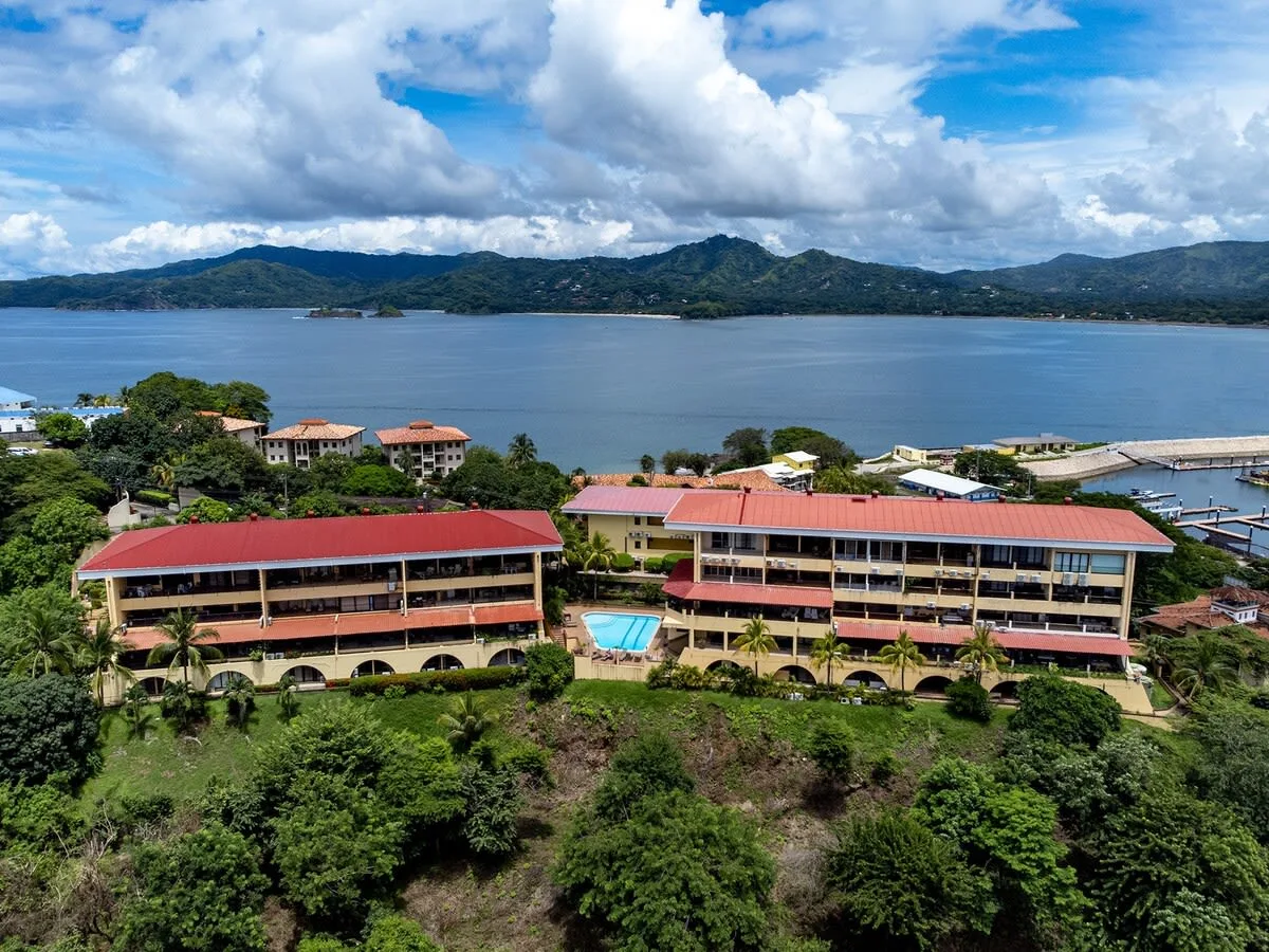 Zona común: Vista aérea de edificios junto a un lago, con colinas verdes a lo lejos.