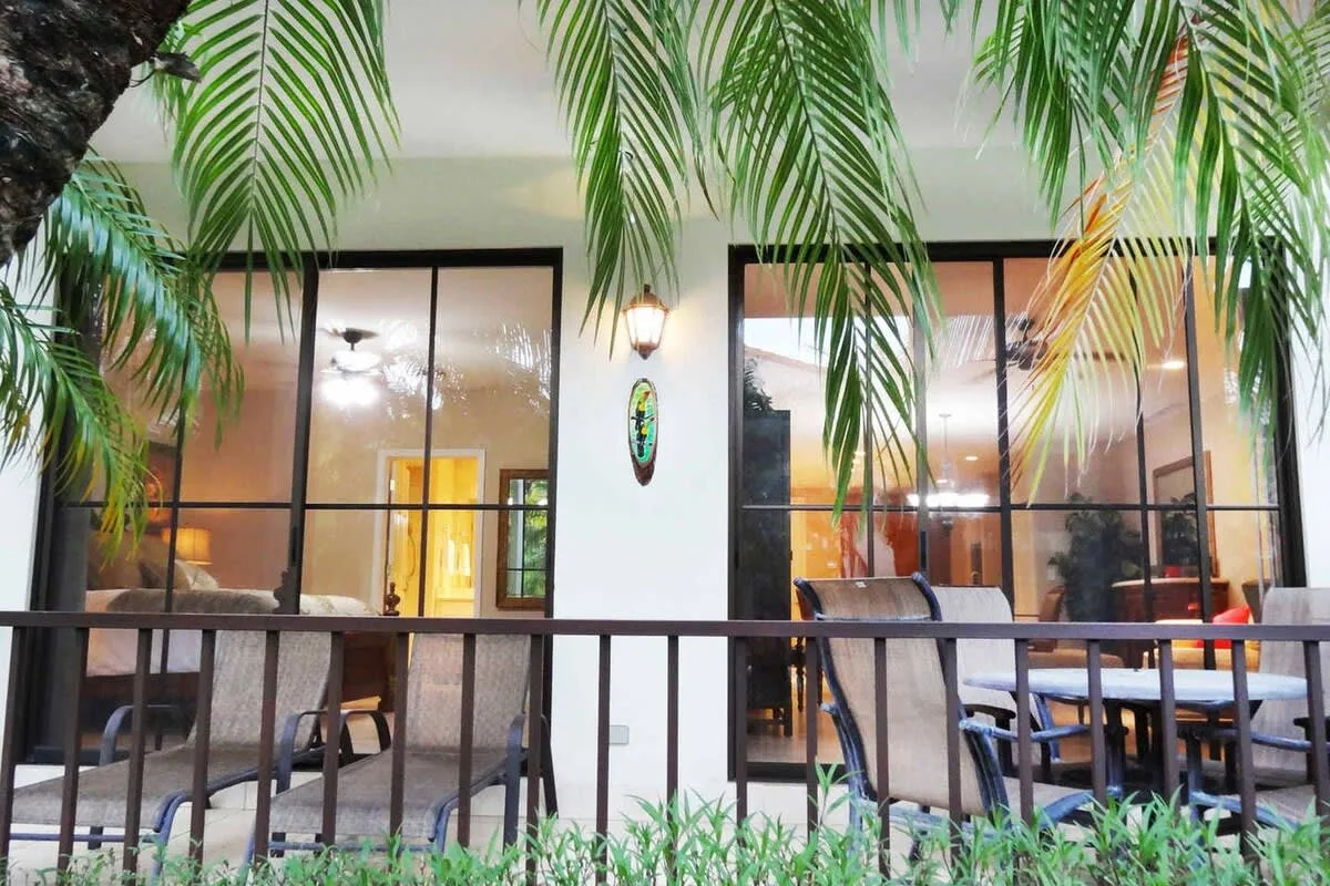 Una zona de asientos en un patio queda detrás de una barandilla negra, con grandes ventanas al fondo.