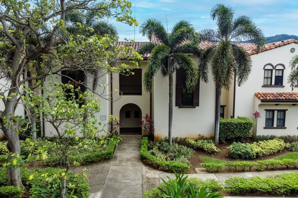 Zona común: Un edificio blanco con entradas arqueadas, palmeras y jardines.