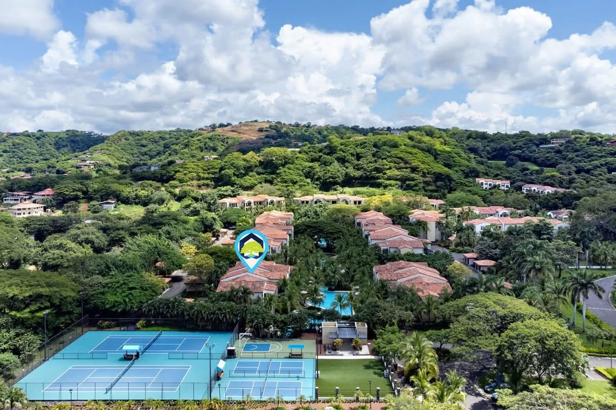 Zona común: Un complejo residencial en una colina domina canchas de tenis rodeadas de vegetación.