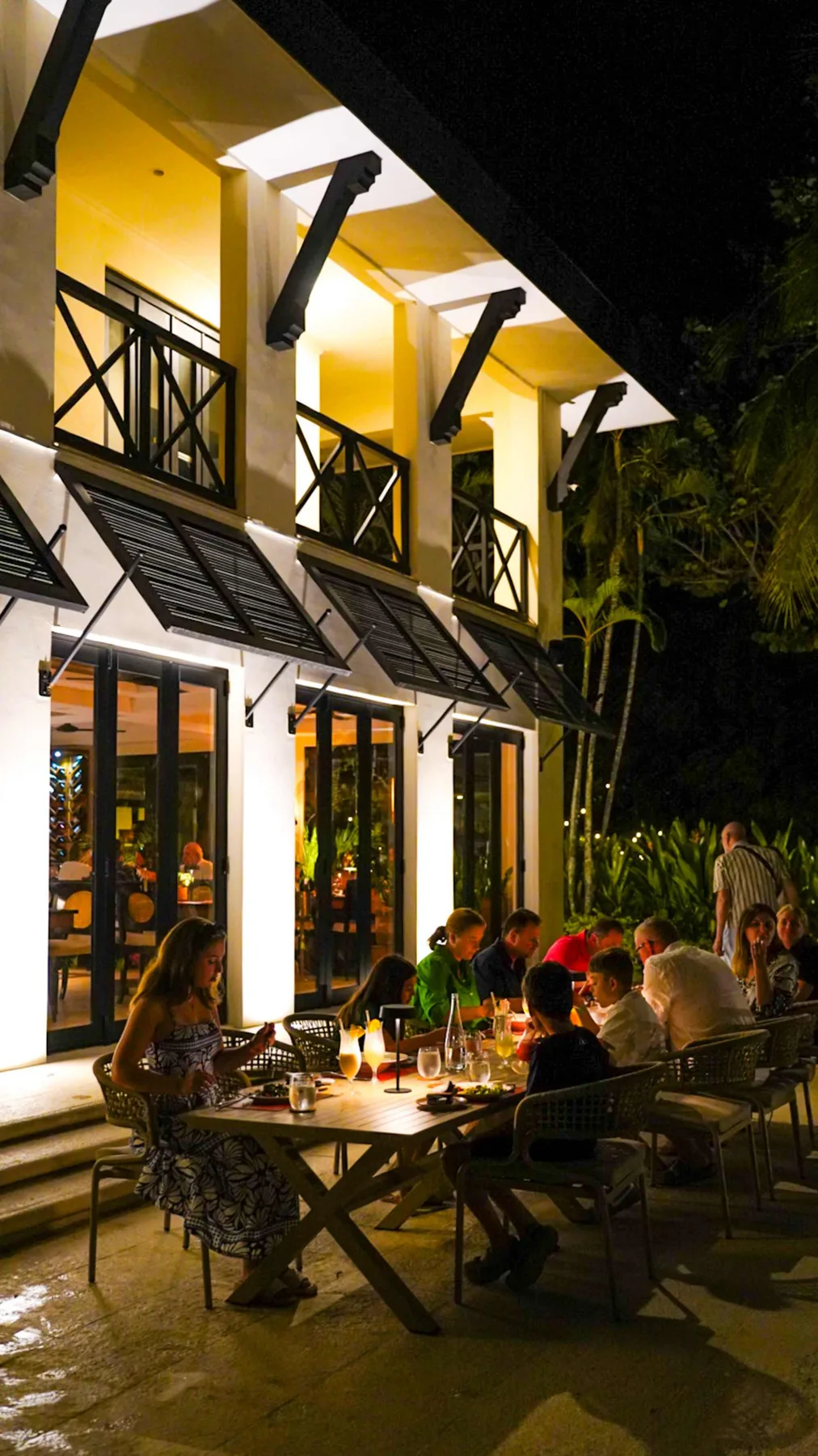 Zona común: Una zona de comedor al aire libre junto a un edificio iluminado, con personas reunidas alrededor de una mesa.