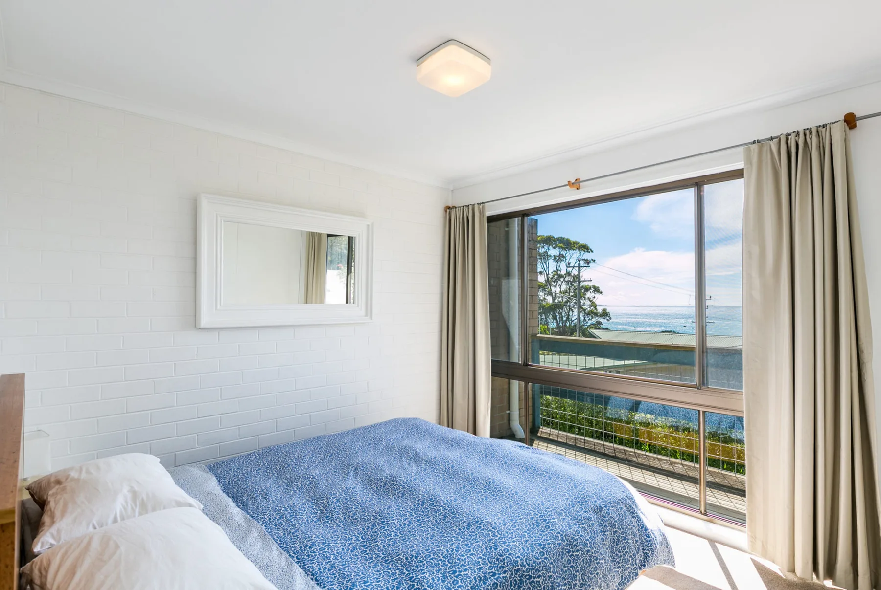 Un dormitorio con una cama junto a una gran ventana con vistas al agua.