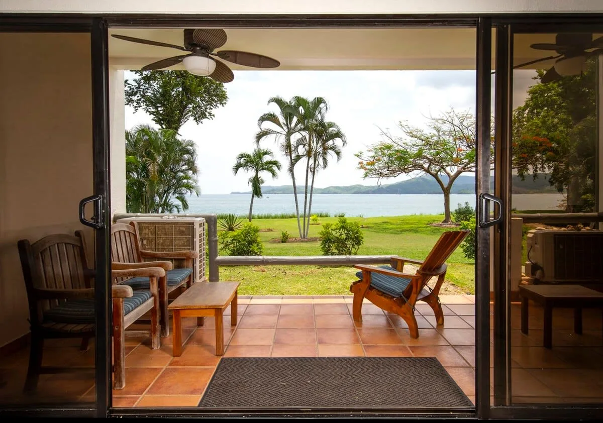 A furnished patio opens onto a green lawn and ocean view.
