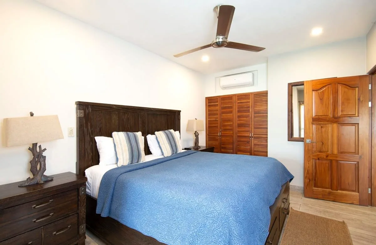 A bedroom with a blue bedspread, wooden headboard, and louvered closet doors.