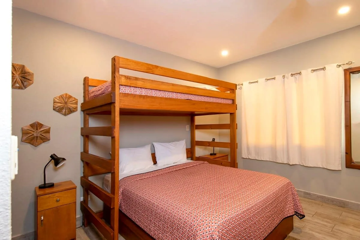 A bedroom with a wooden bunk bed, a made bed, and white curtains.