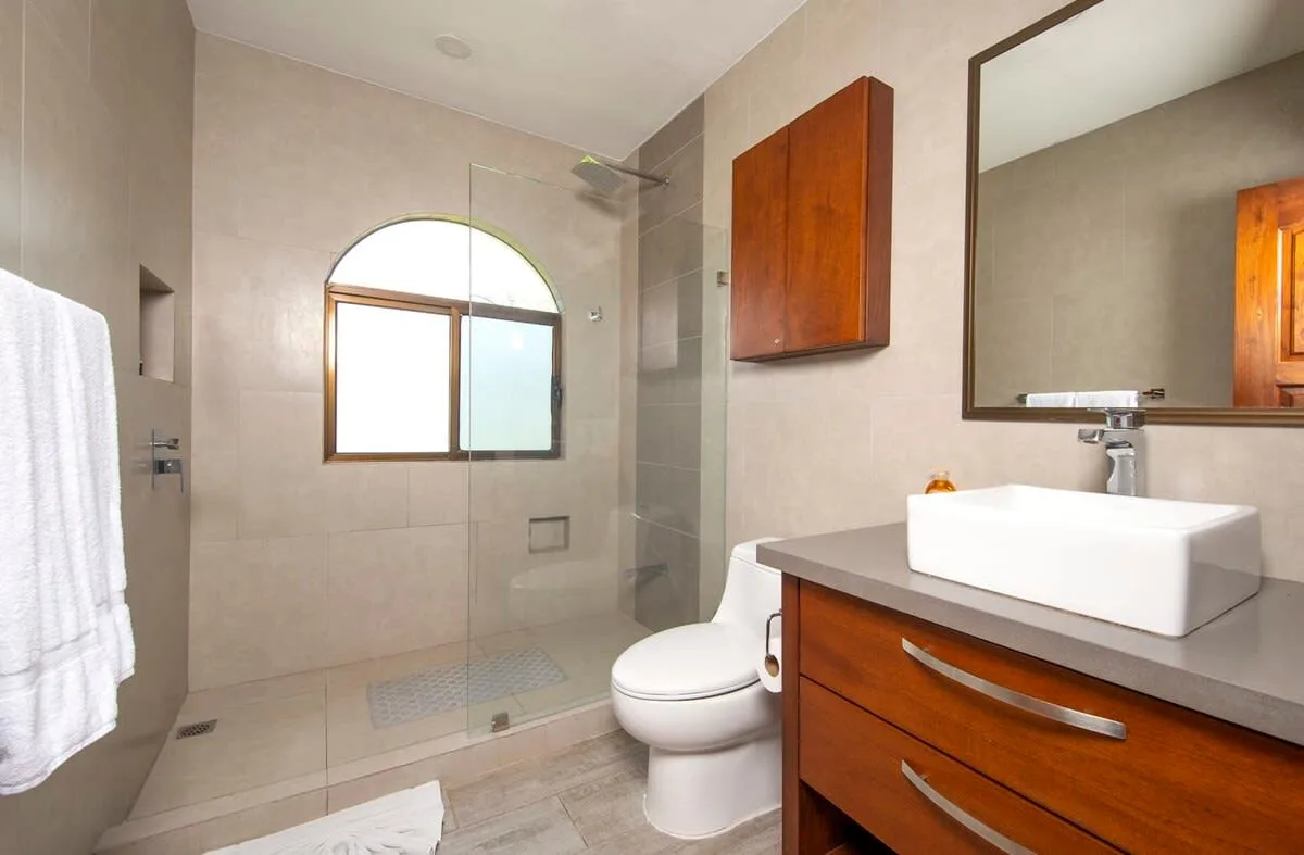 A bathroom with a glass shower, toilet, and wooden vanity.