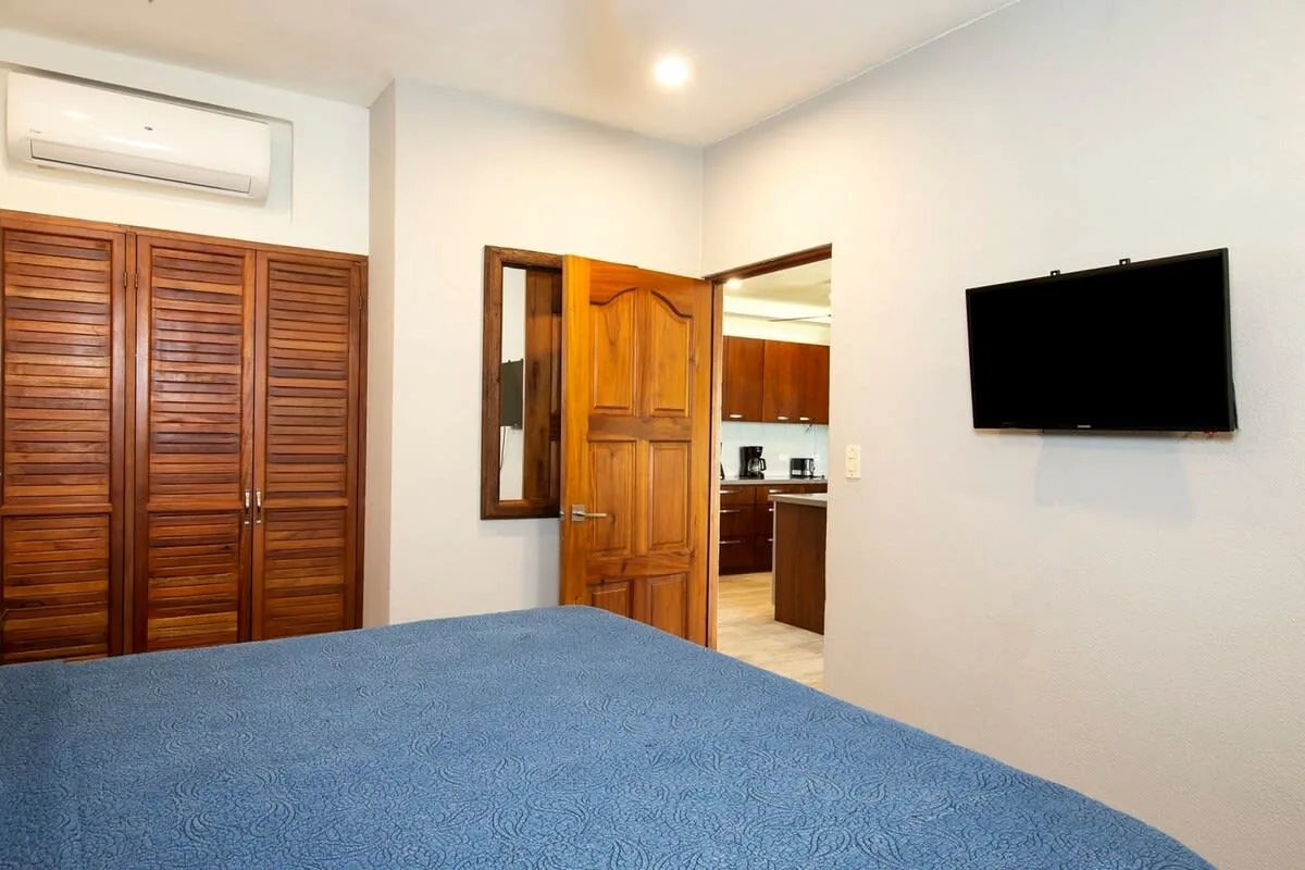 Bedroom with a blue bedspread, wooden wardrobes, and a wall-mounted television.