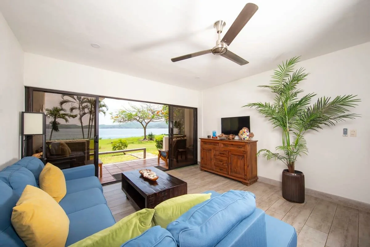 A bright living room opens onto a patio, with blue seating and a ceiling fan.