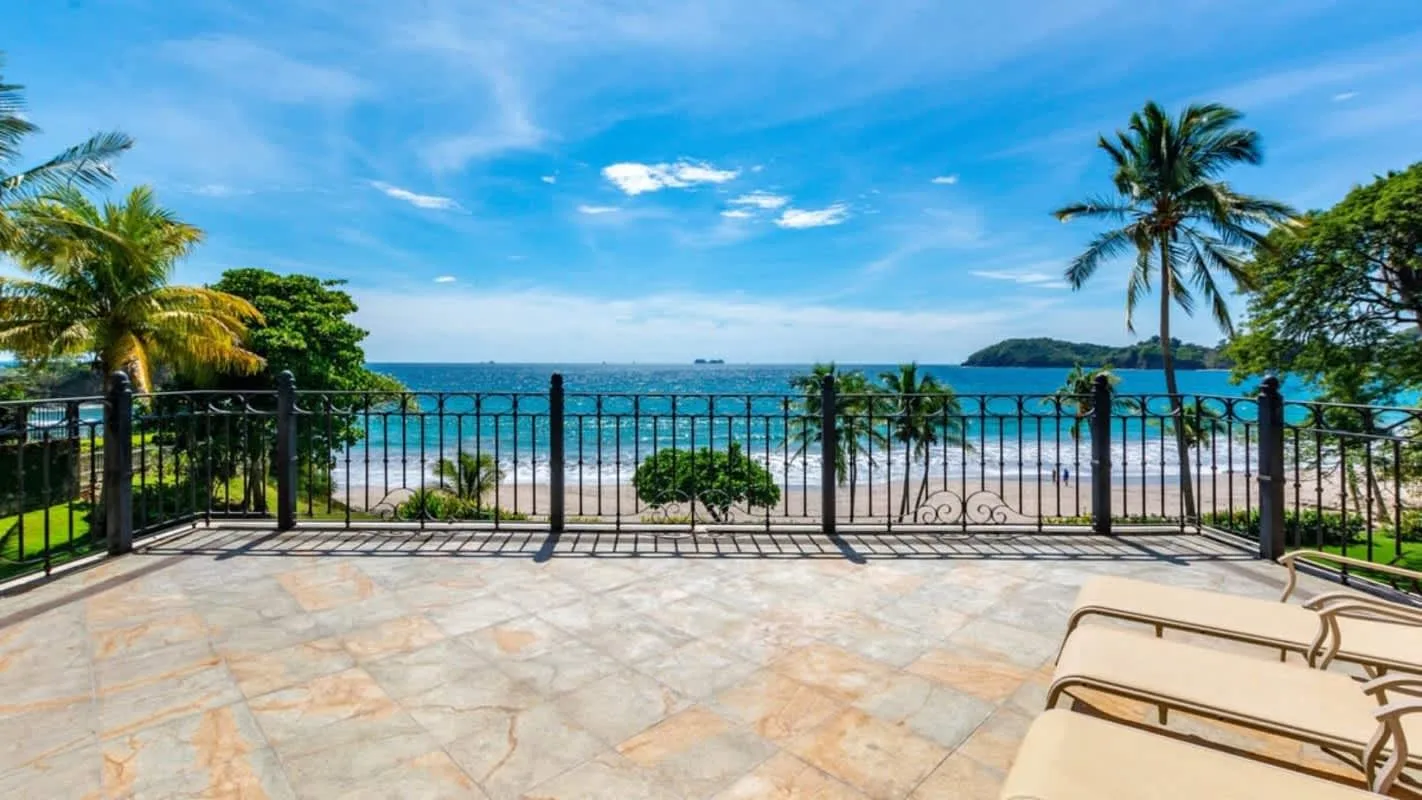 A seaside patio overlooks the beach and ocean beyond a railing.