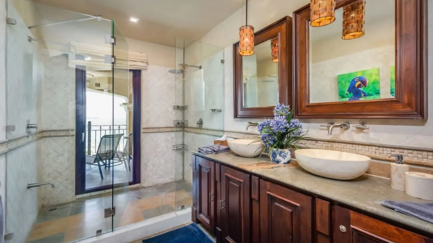 A bathroom with a glass shower, double sinks, and wooden vanity cabinets.