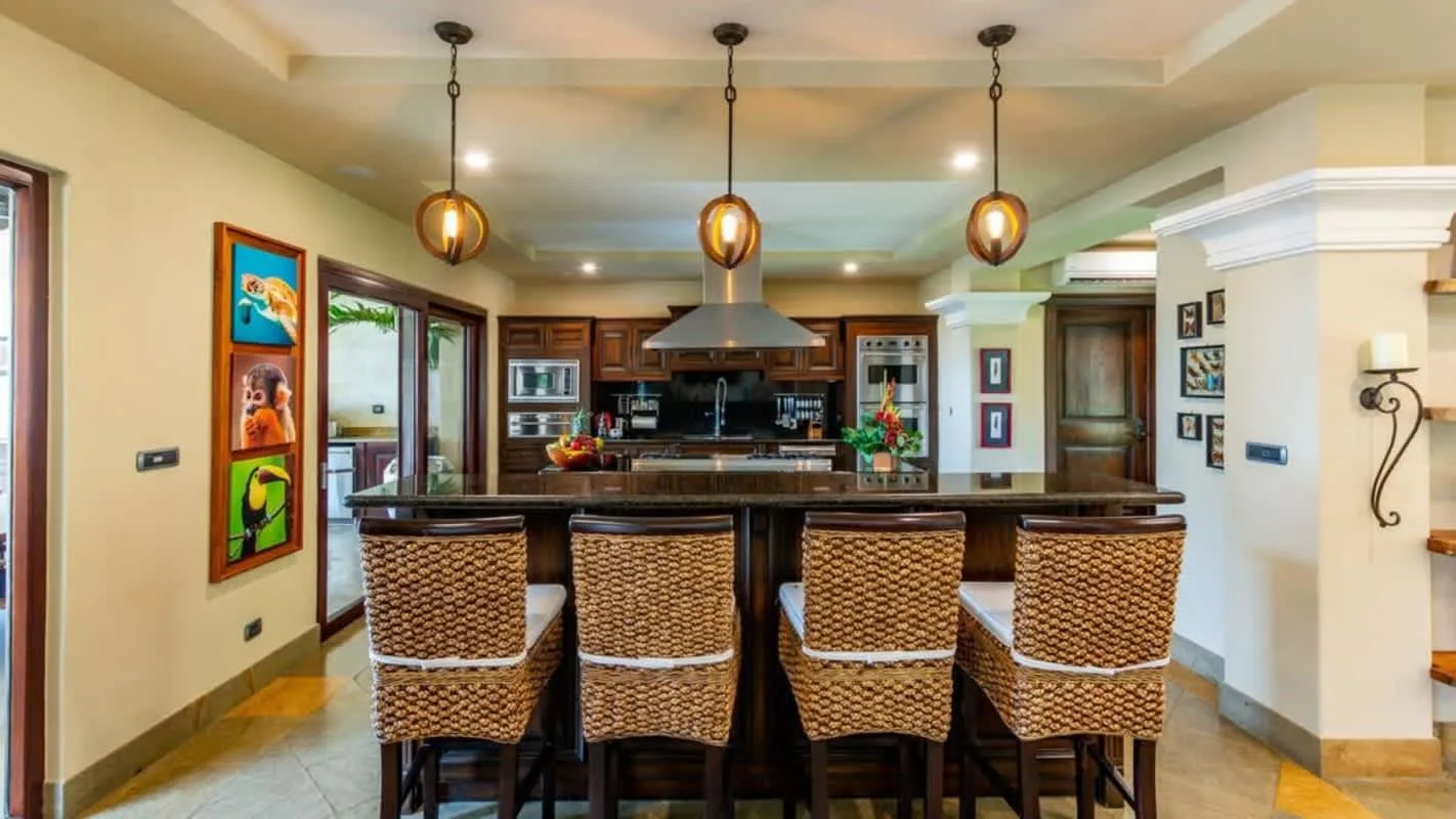 A kitchen island with woven seating sits beneath pendant lights.