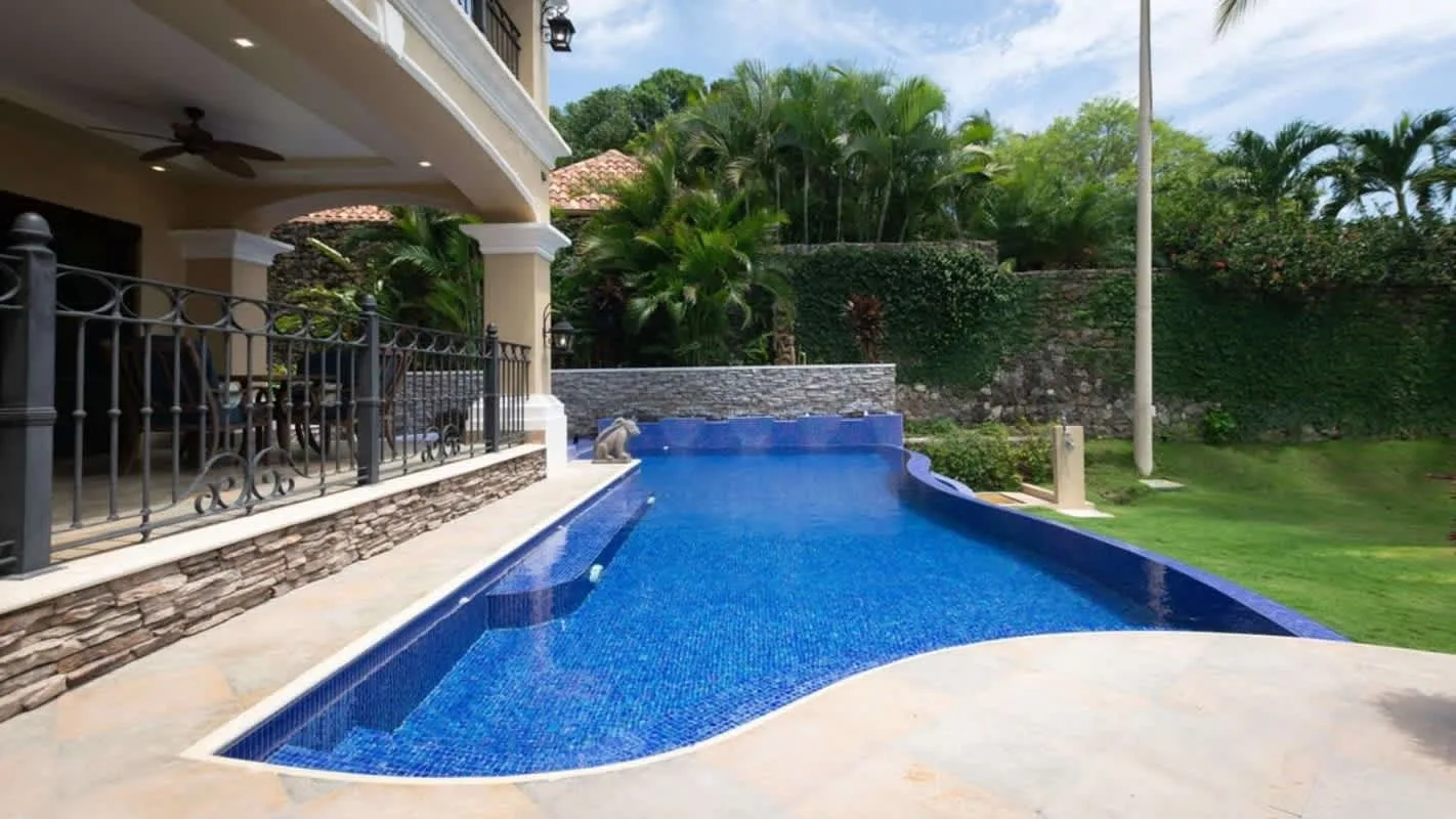 An outdoor swimming pool beside a covered patio and landscaped garden.