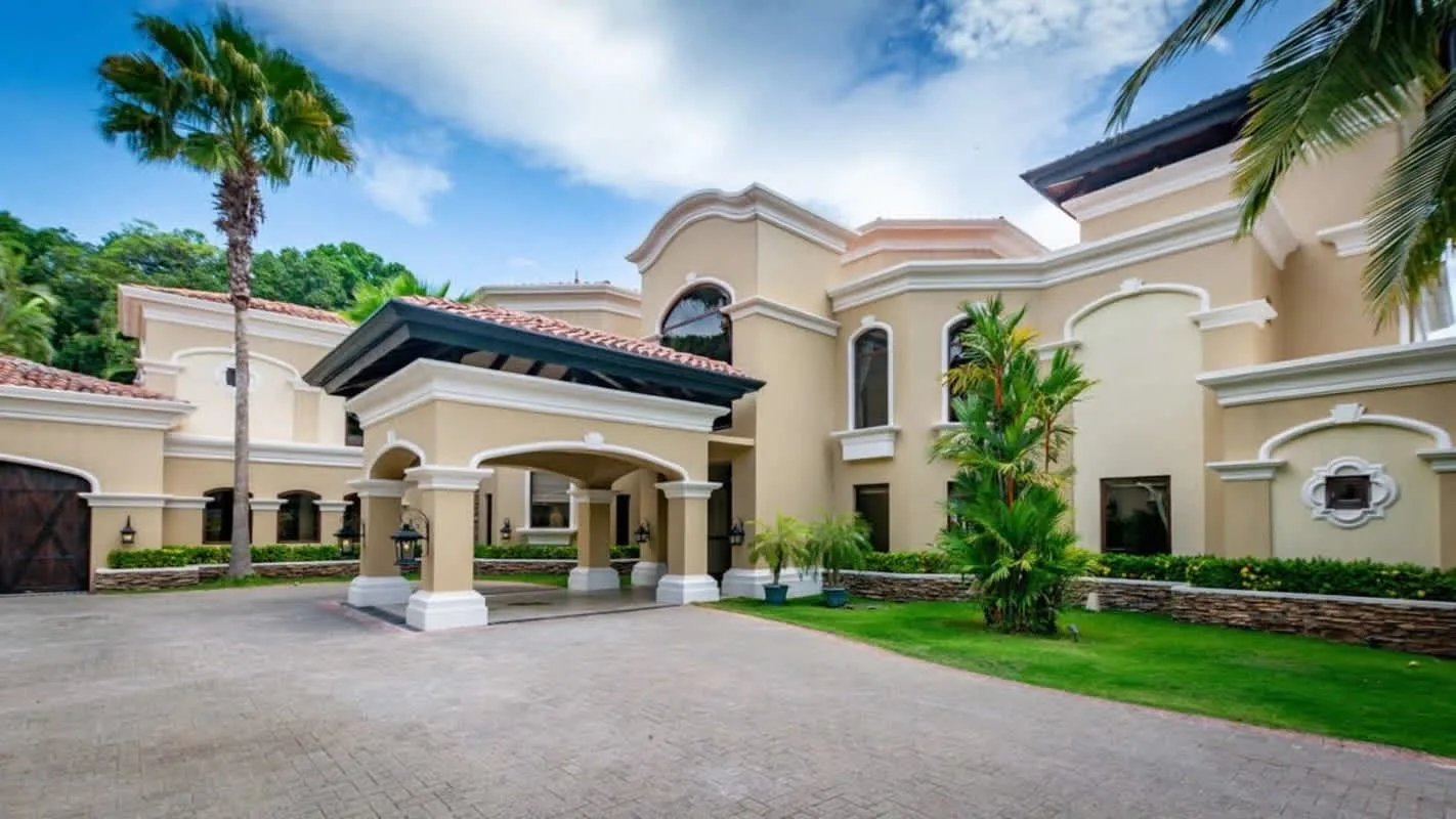 A large cream-colored building stands beside a paved driveway and landscaped grounds.