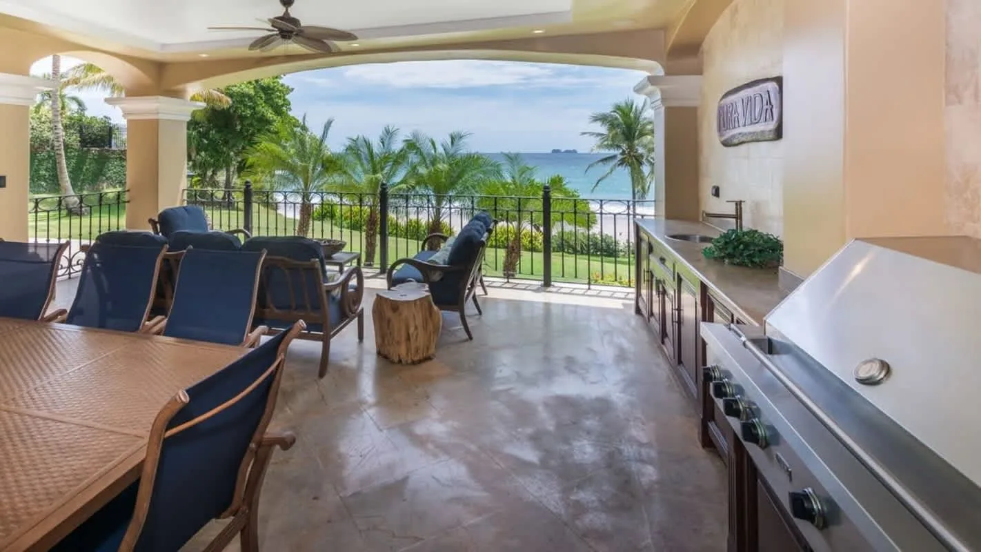 A covered patio overlooks the ocean, with dining seating and a built-in grill.