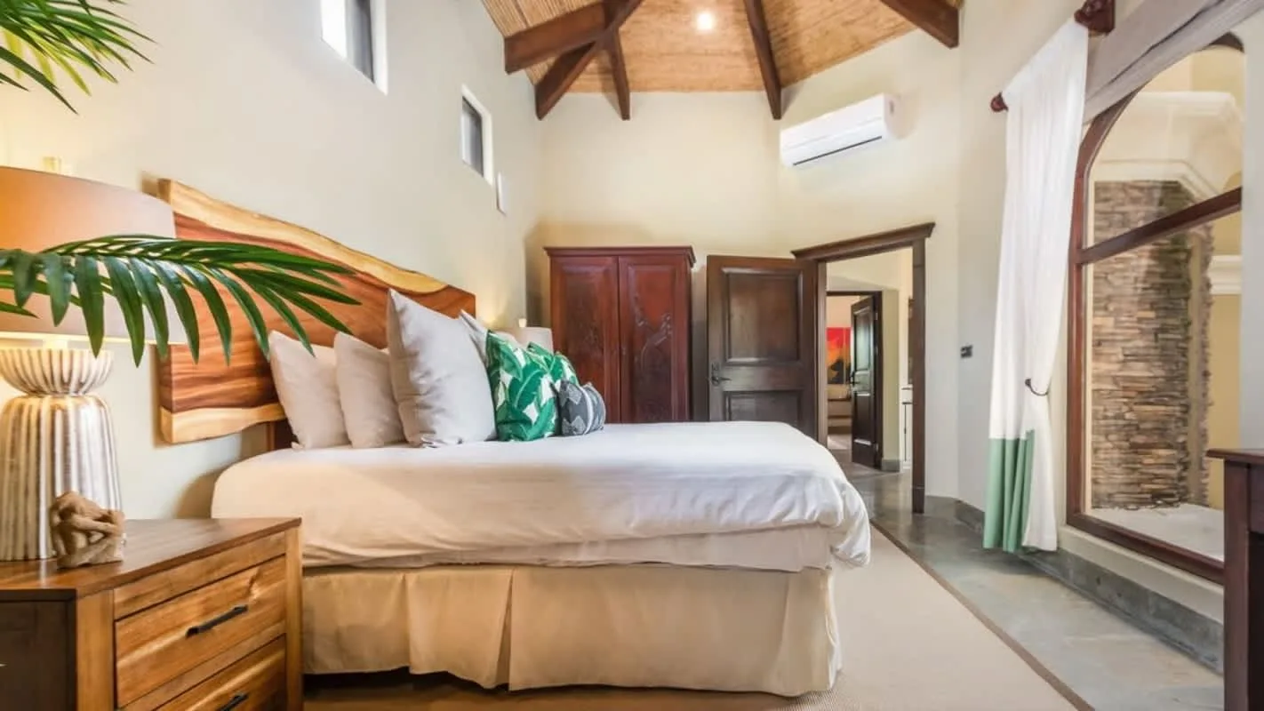 A bedroom with a bed, wooden ceiling beams, and glass doors opening to a patio.